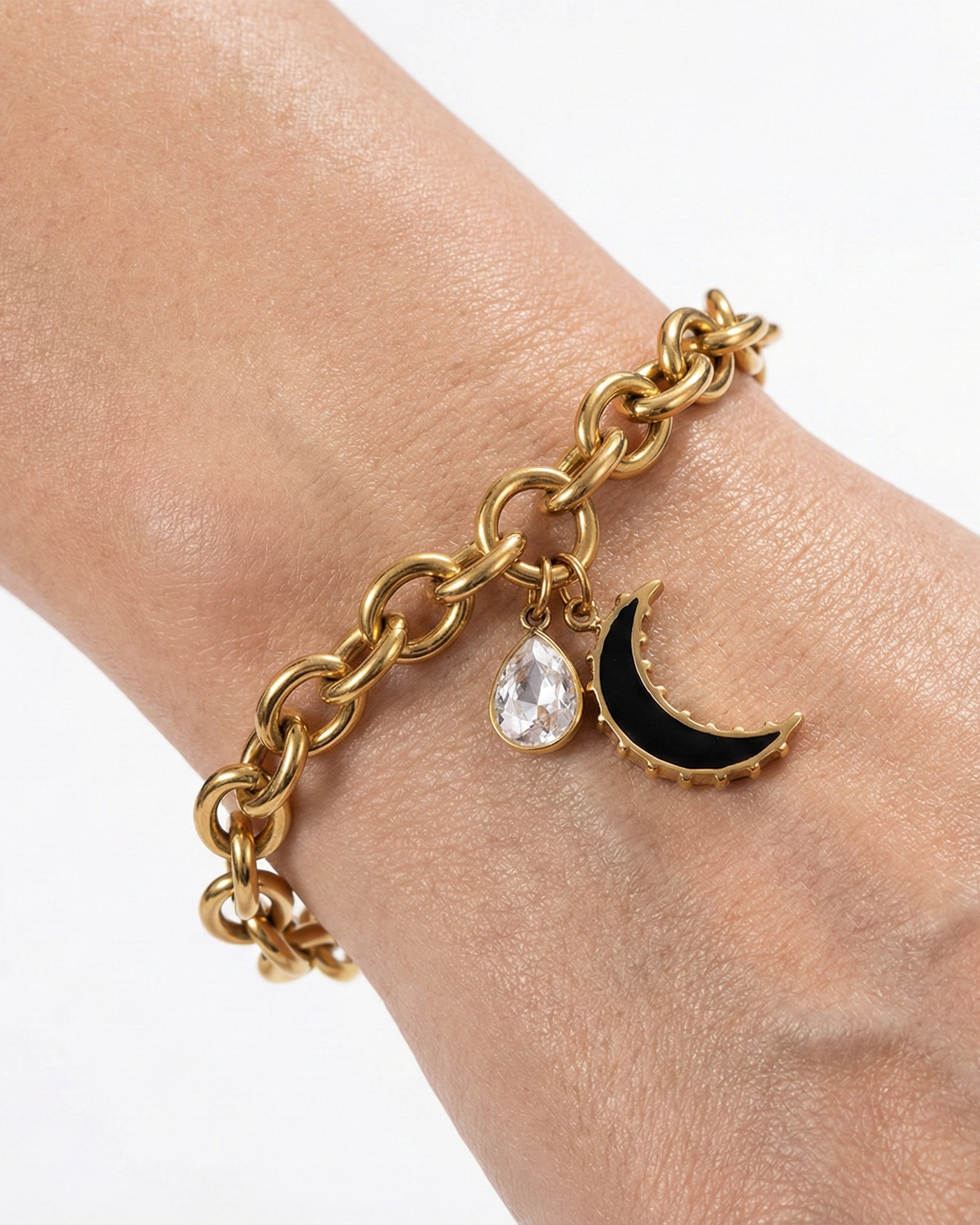 Gold chain bracelet with a moon and teardrop charm on a wrist against a white background