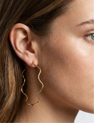 Close-up of a person wearing gold hoop earrings with a blurred background