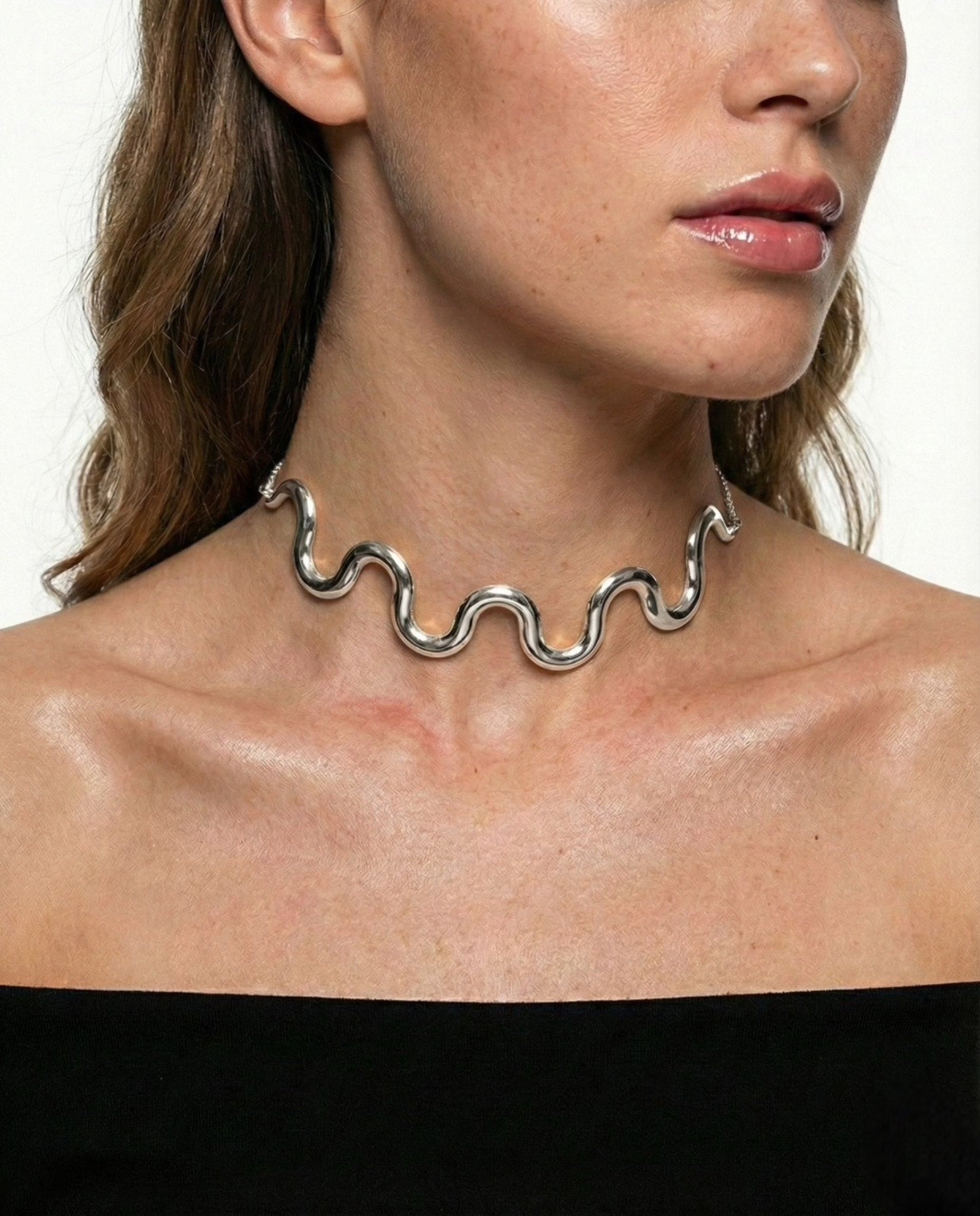 Woman wearing a wavy silver necklace against a white background