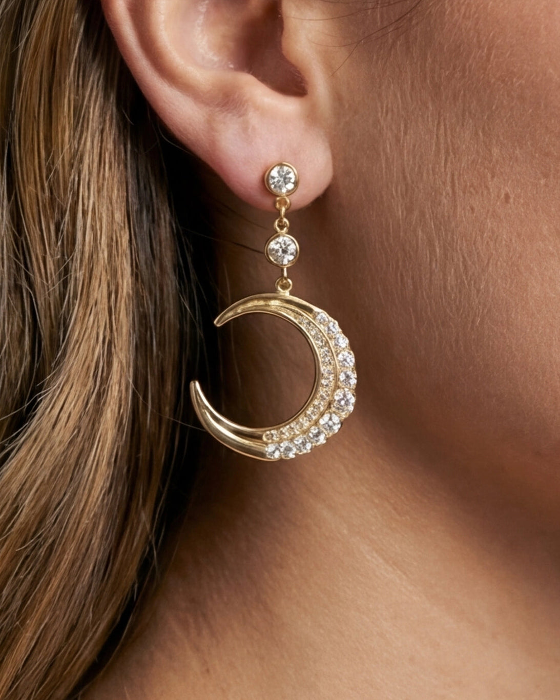 Gold crescent moon earring with clear stones worn by a person.