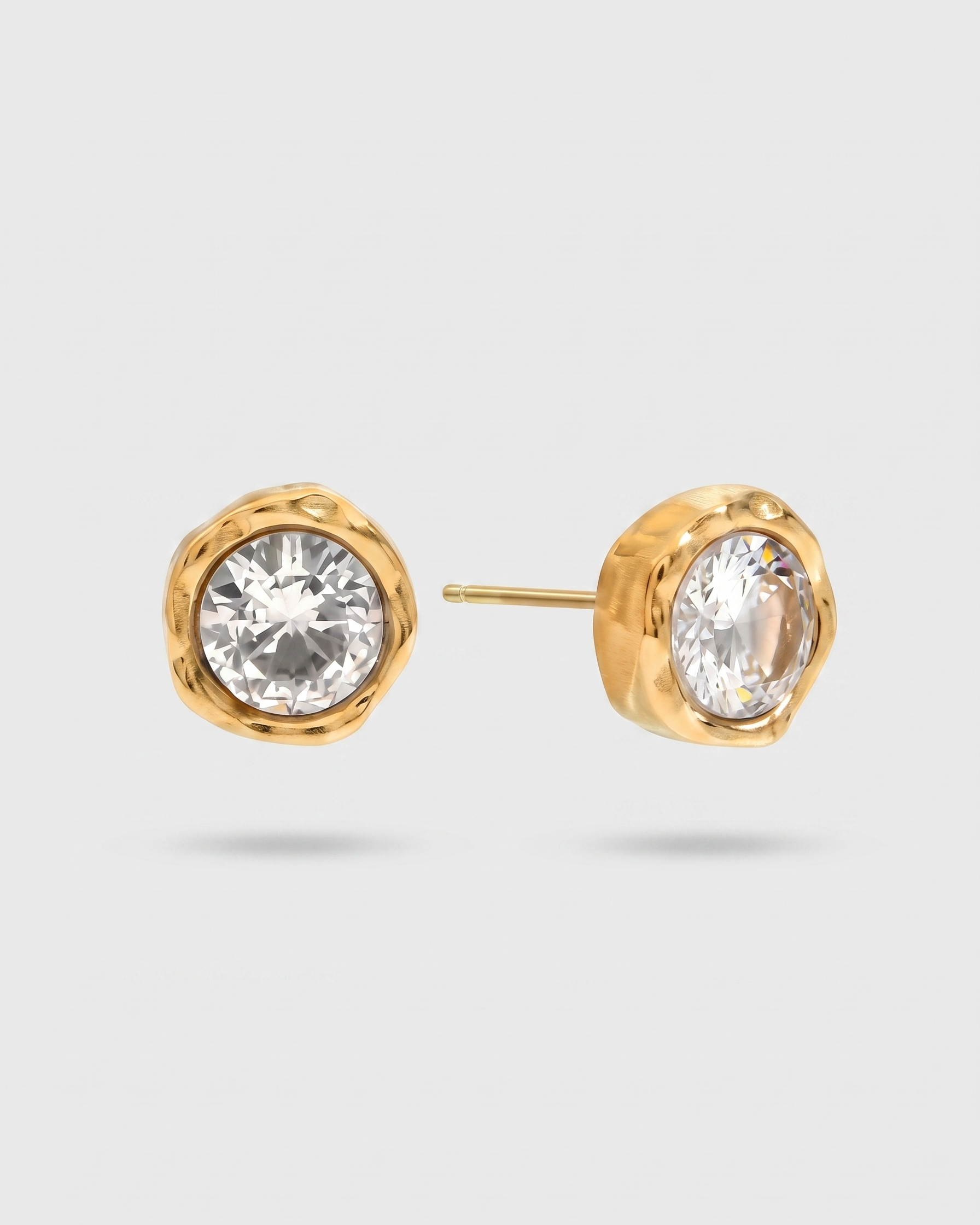 Gold stud earrings with clear gemstones on a light gray background