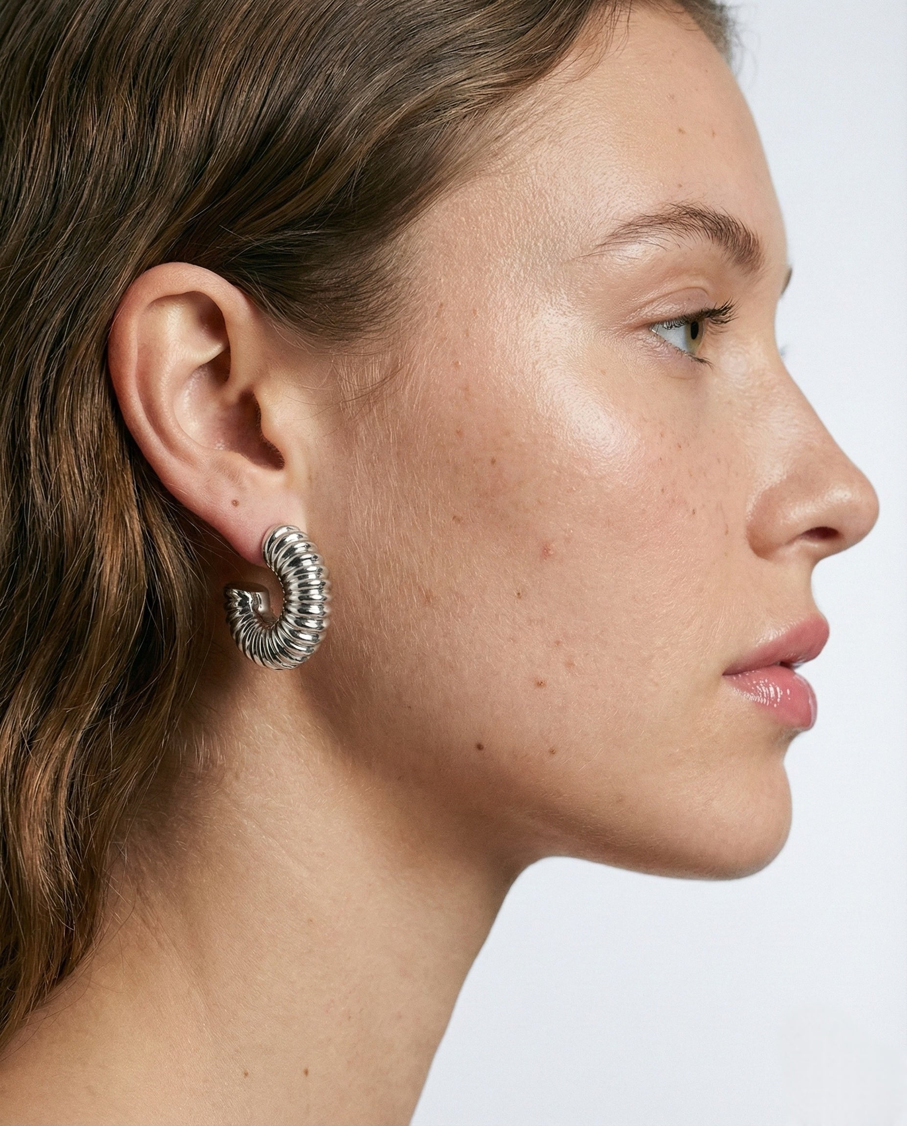 Close-up of a person wearing a silver hoop earring on a plain background