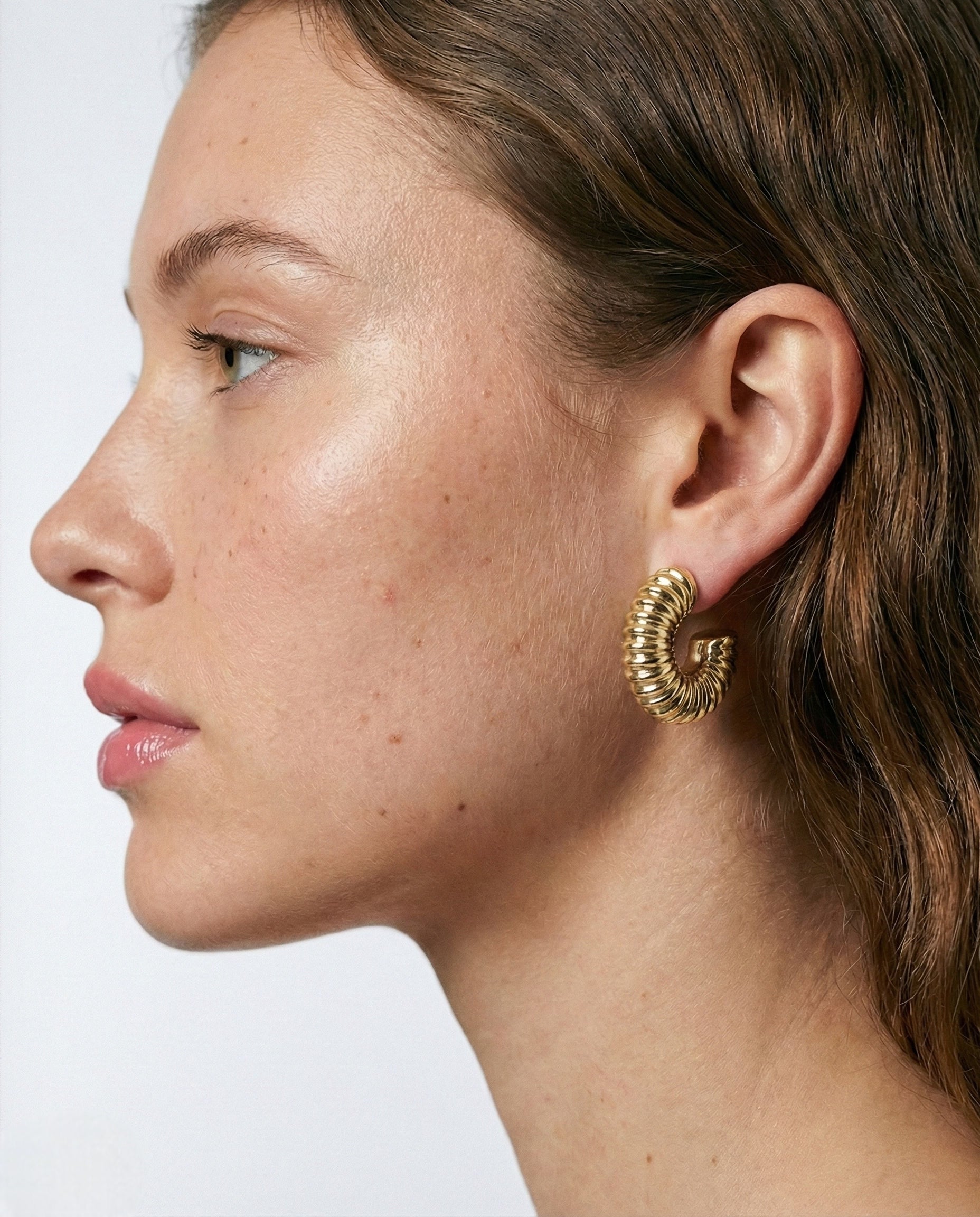 Close-up of a person wearing gold hoop earrings on a plain background