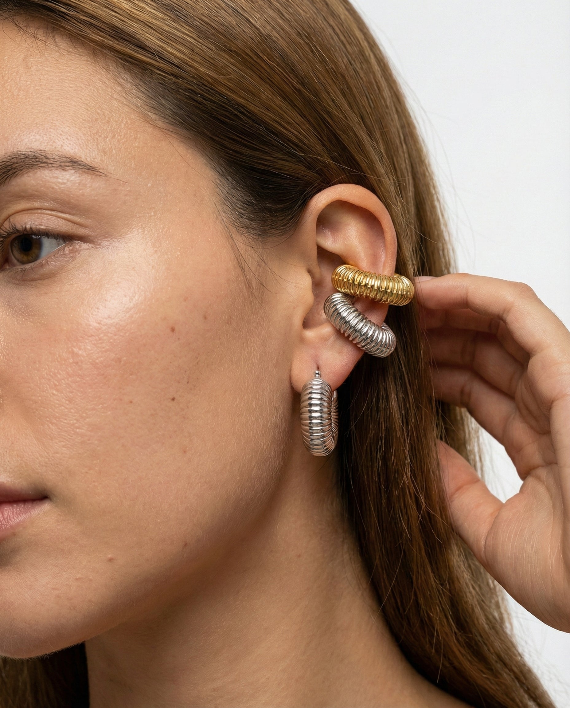 Close-up of a woman's ear with gold and silver hoop earrings against a neutral background