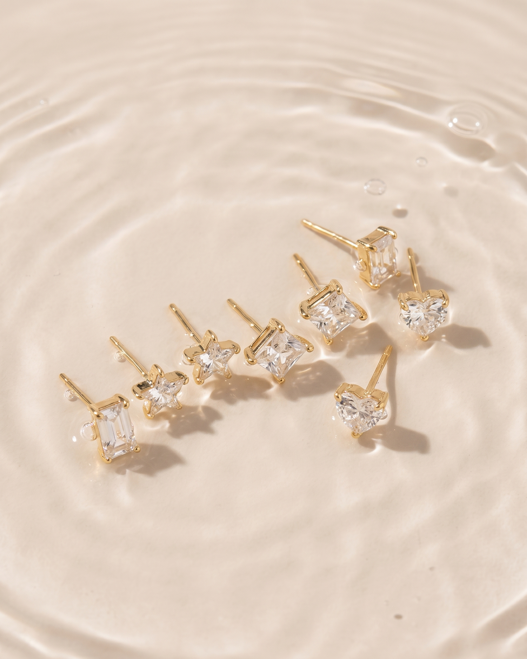 Gold earrings with clear gemstones on a water surface