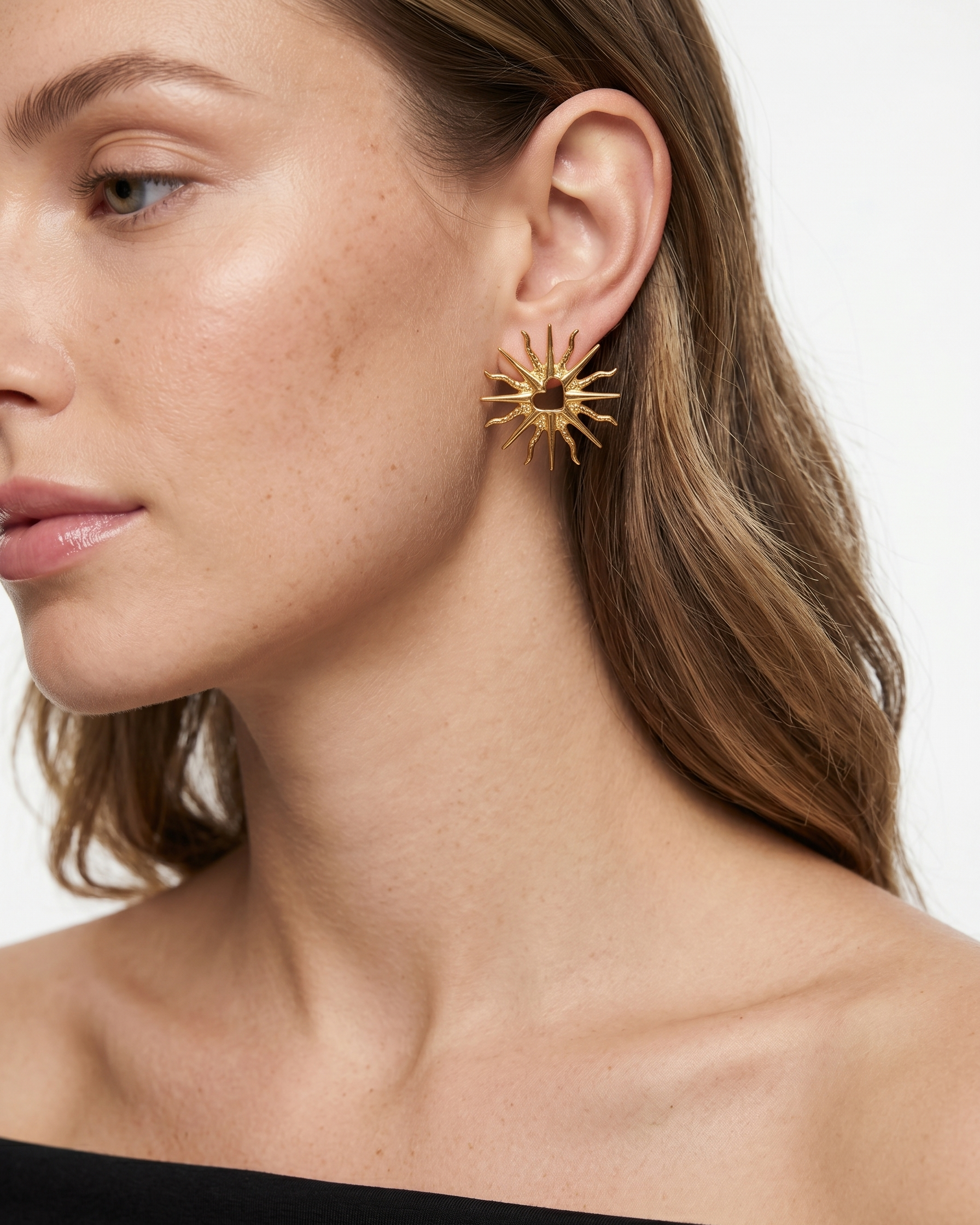 Close-up of a woman wearing gold earrings with a plain background