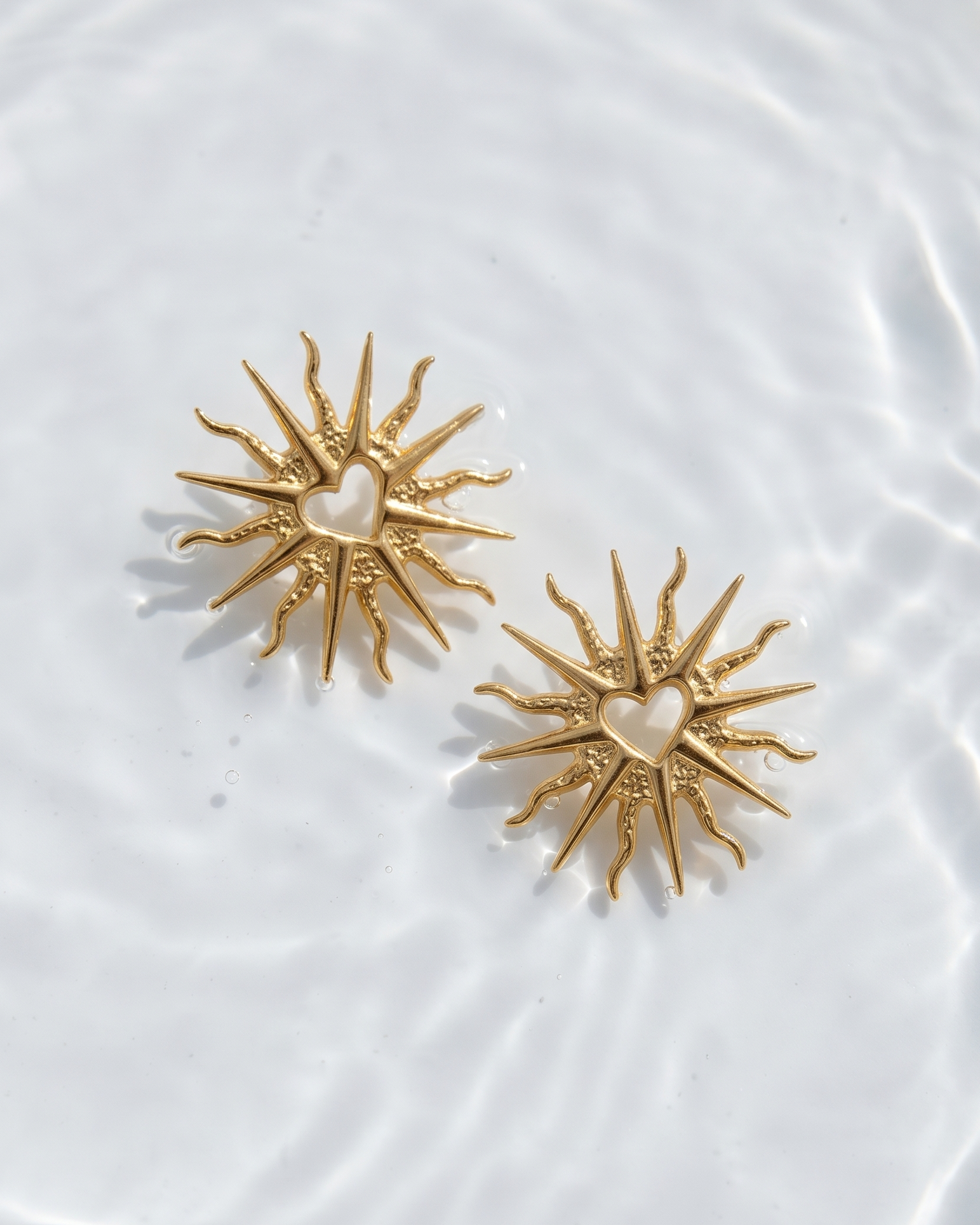 Gold sun-shaped earrings with a heart center on a white textured background