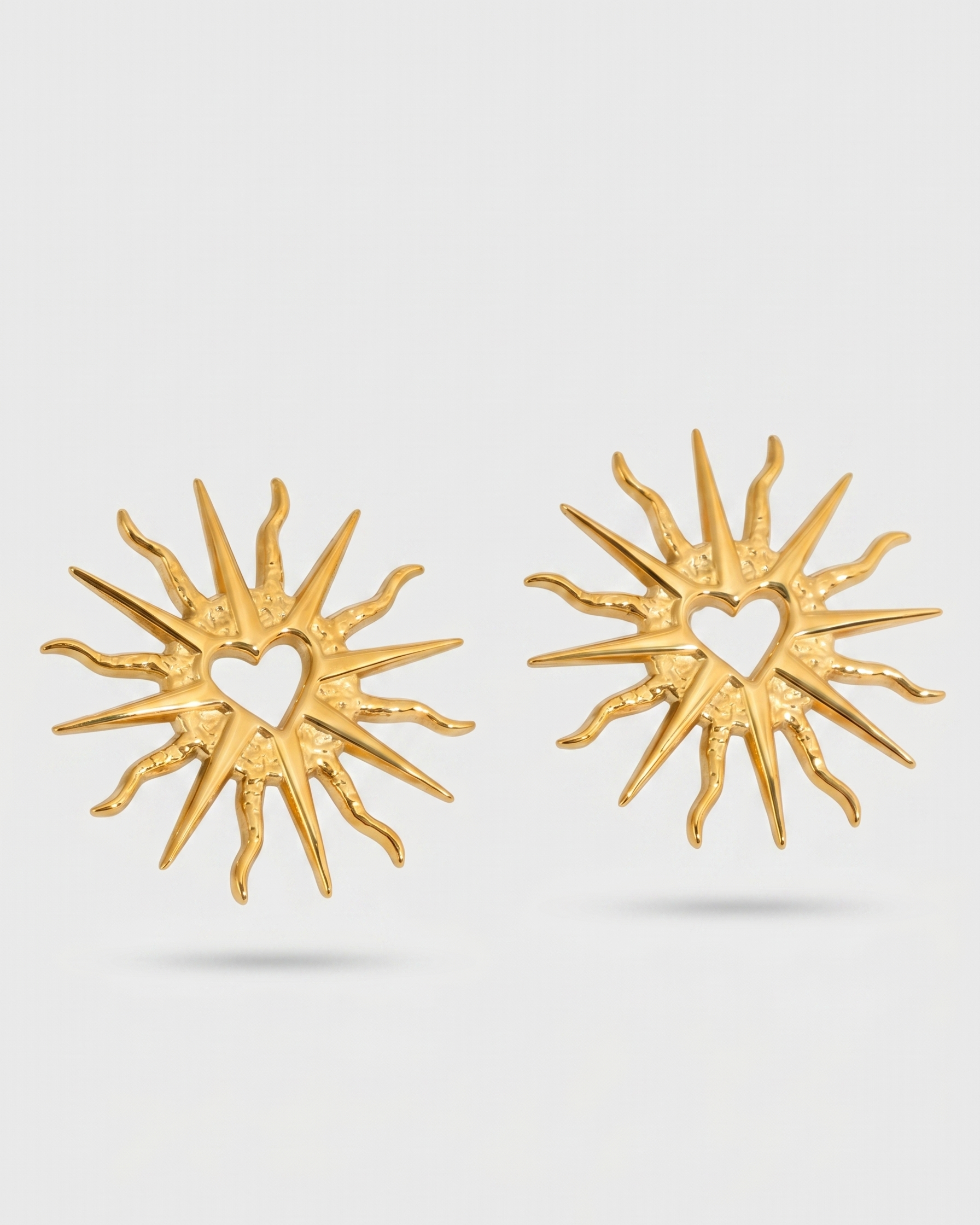 Gold sun-shaped earrings on a light gray background