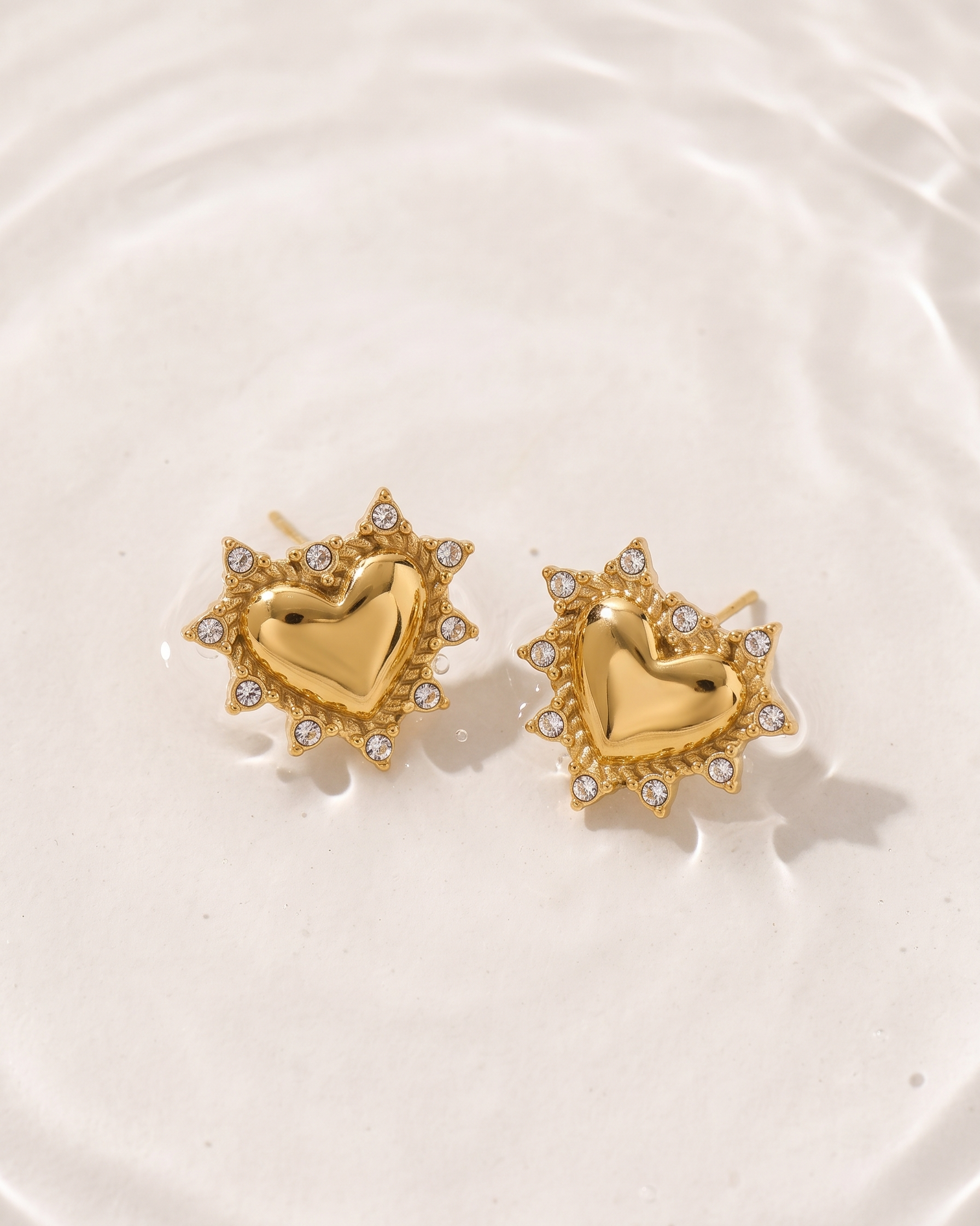 Gold heart-shaped earrings with embedded stones on a white plate