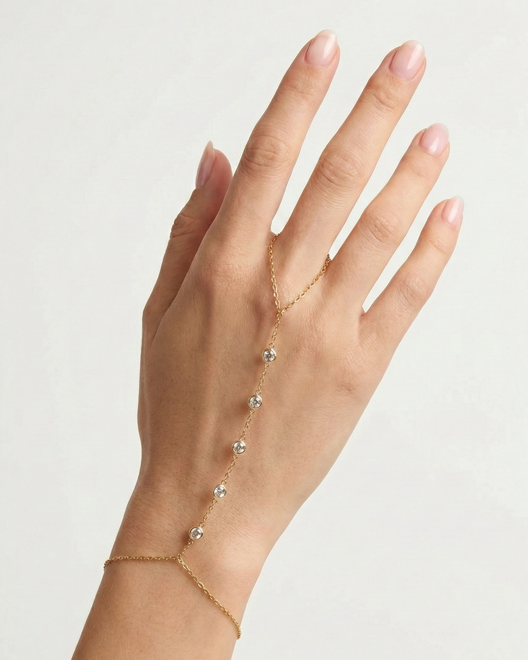 Hand wearing a delicate gold bracelet on a plain background