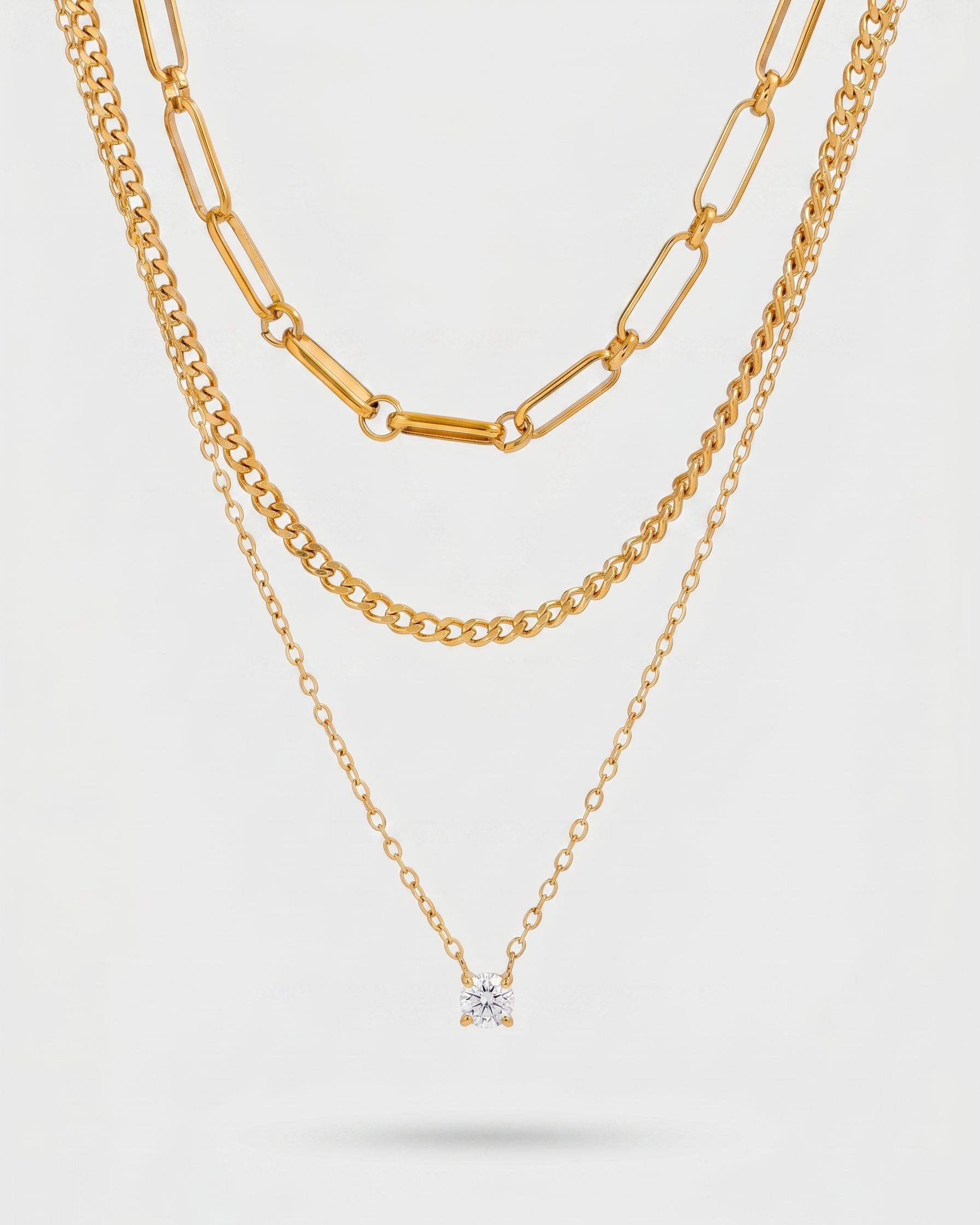 Three gold necklaces on a light gray background