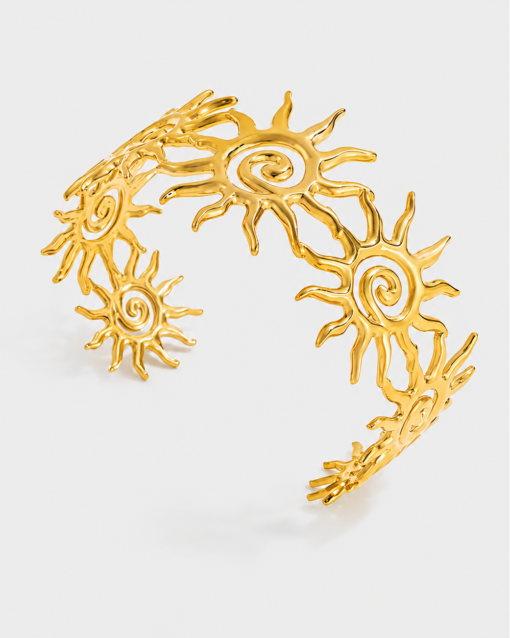 A gold-toned open cuff bangle decorated with multiple stylized sun motifs, photographed on a clean light gray background.