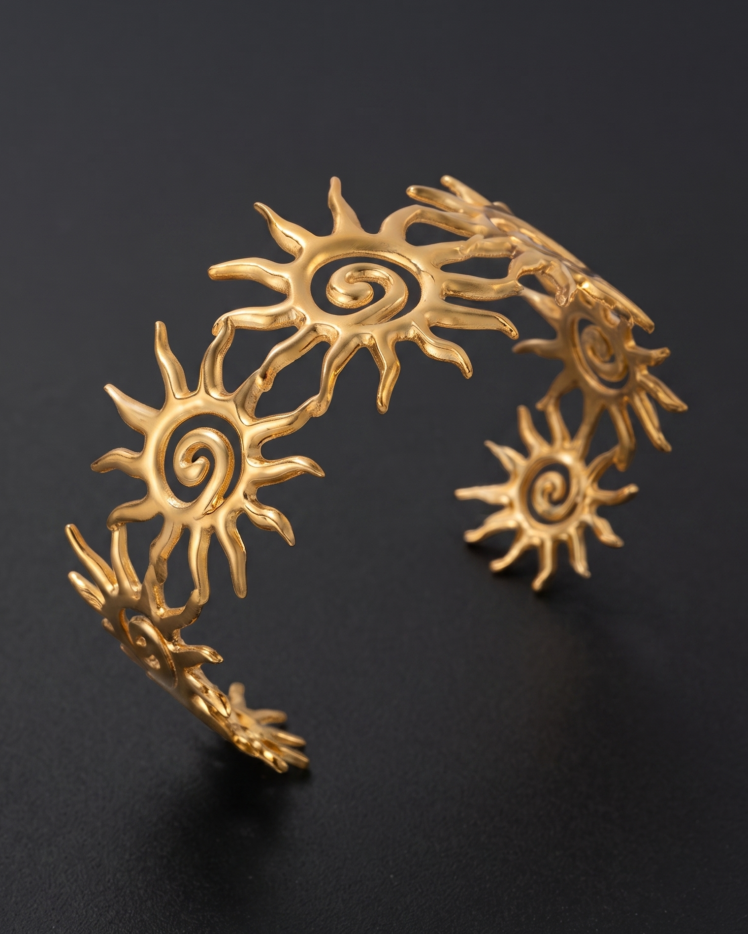 A gold-toned metal cuff bracelet featuring multiple sunburst motifs with spiral centers, displayed on a dark black background.