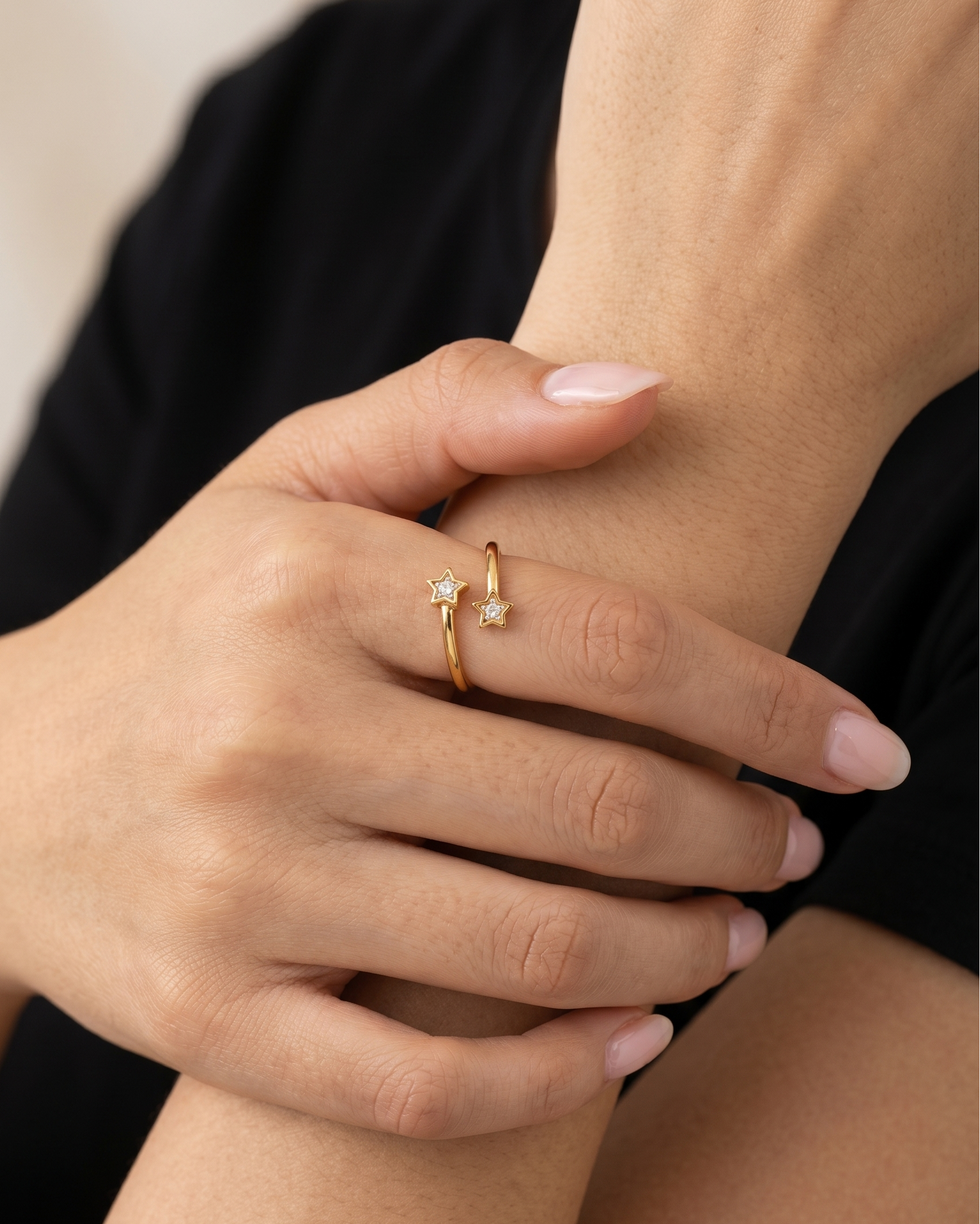 Close-up of a hand wearing a gold ring with two small diamonds on a neutral background
