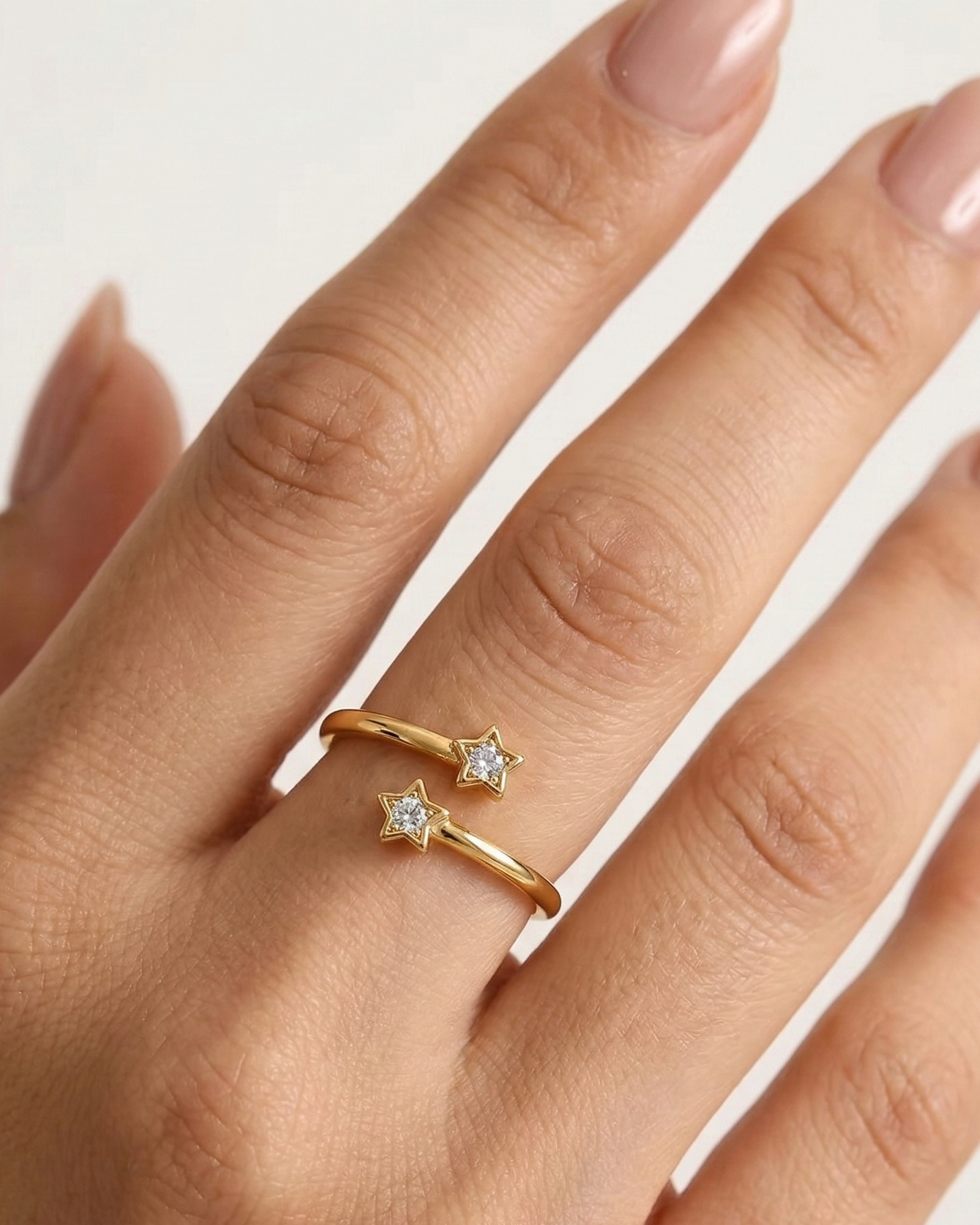 Gold ring with two small diamonds on a hand with light pink nail polish.