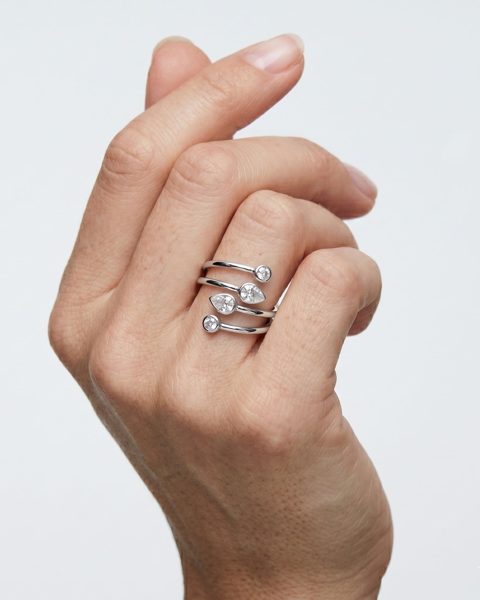 Hand wearing a stack of silver heart-shaped rings on a light gray background