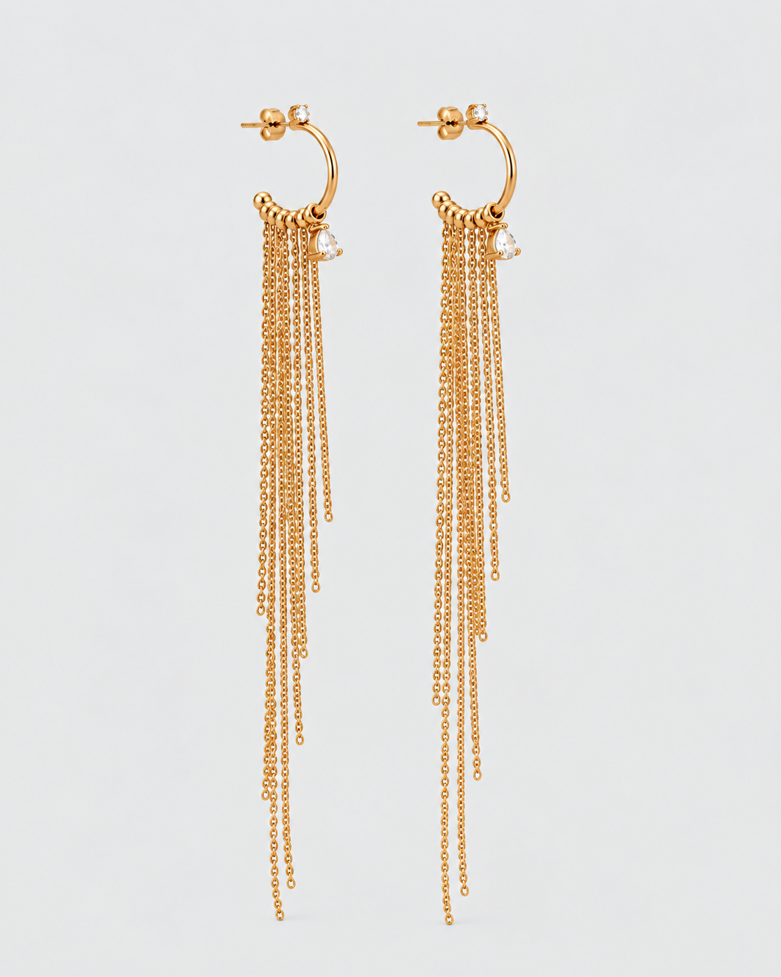 A pair of gold huggie hoop dangle earrings with multiple cascading chain strands and small clear crystal accents, shown against a light gray background.