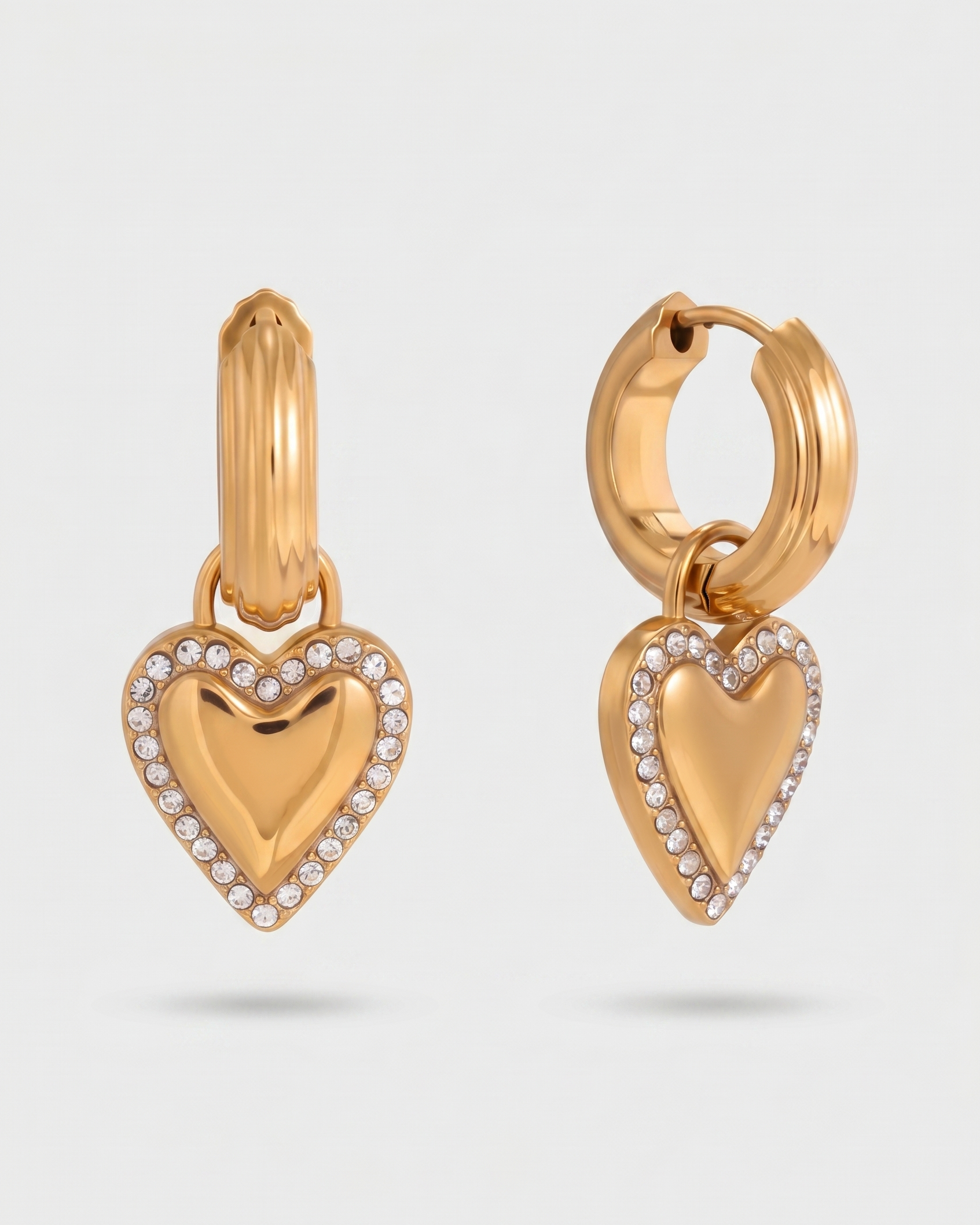 Gold heart-shaped earrings with small diamonds on a light gray background
