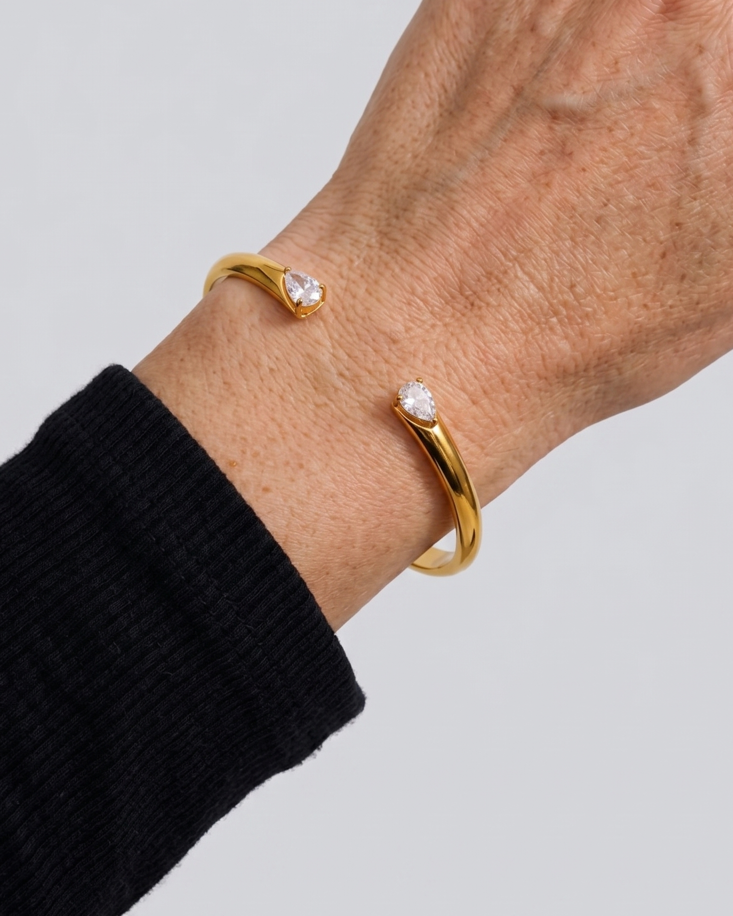 Gold bracelet with heart-shaped gemstones on a wrist against a light gray background
