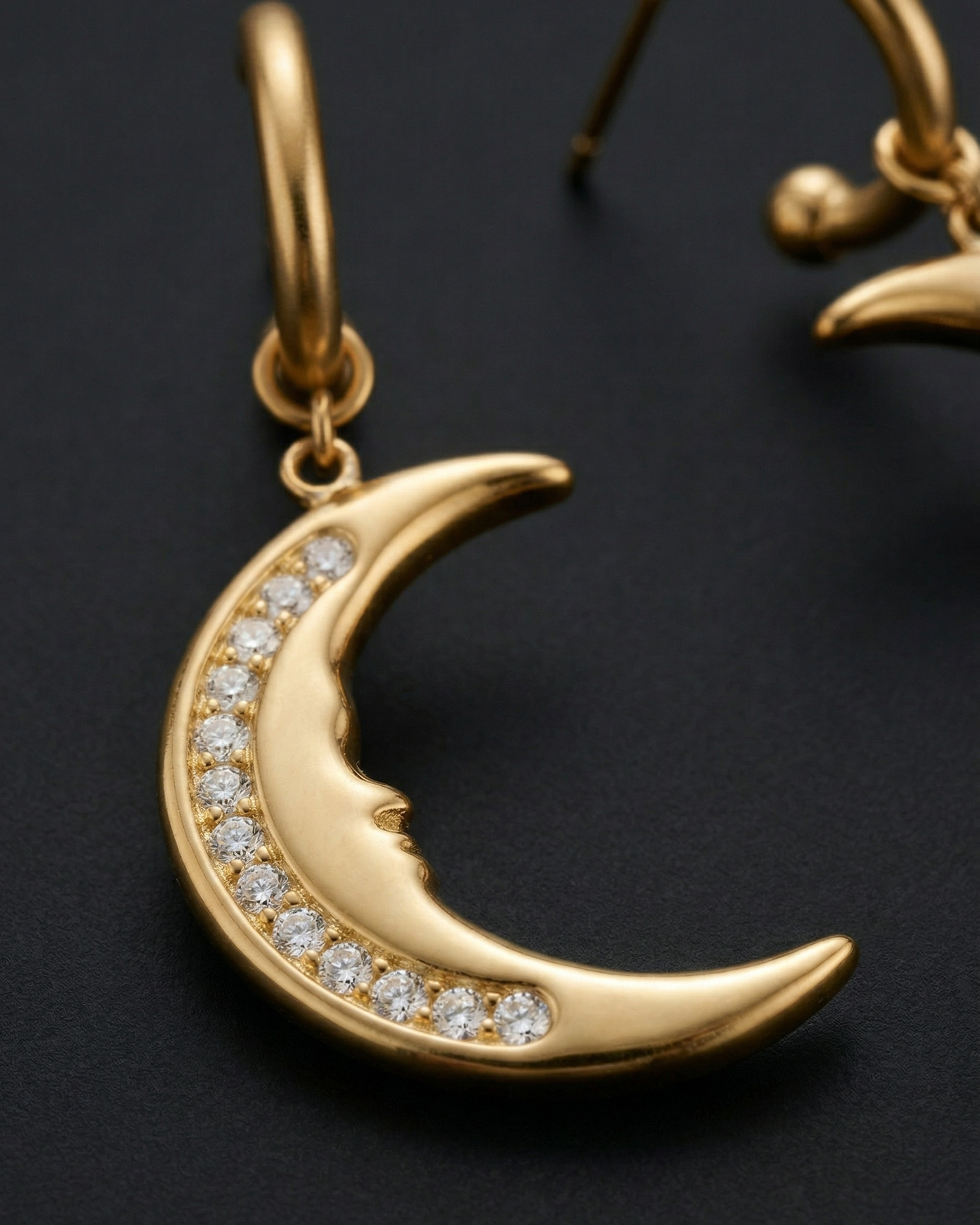 Gold crescent moon earring with embedded diamonds on a dark background