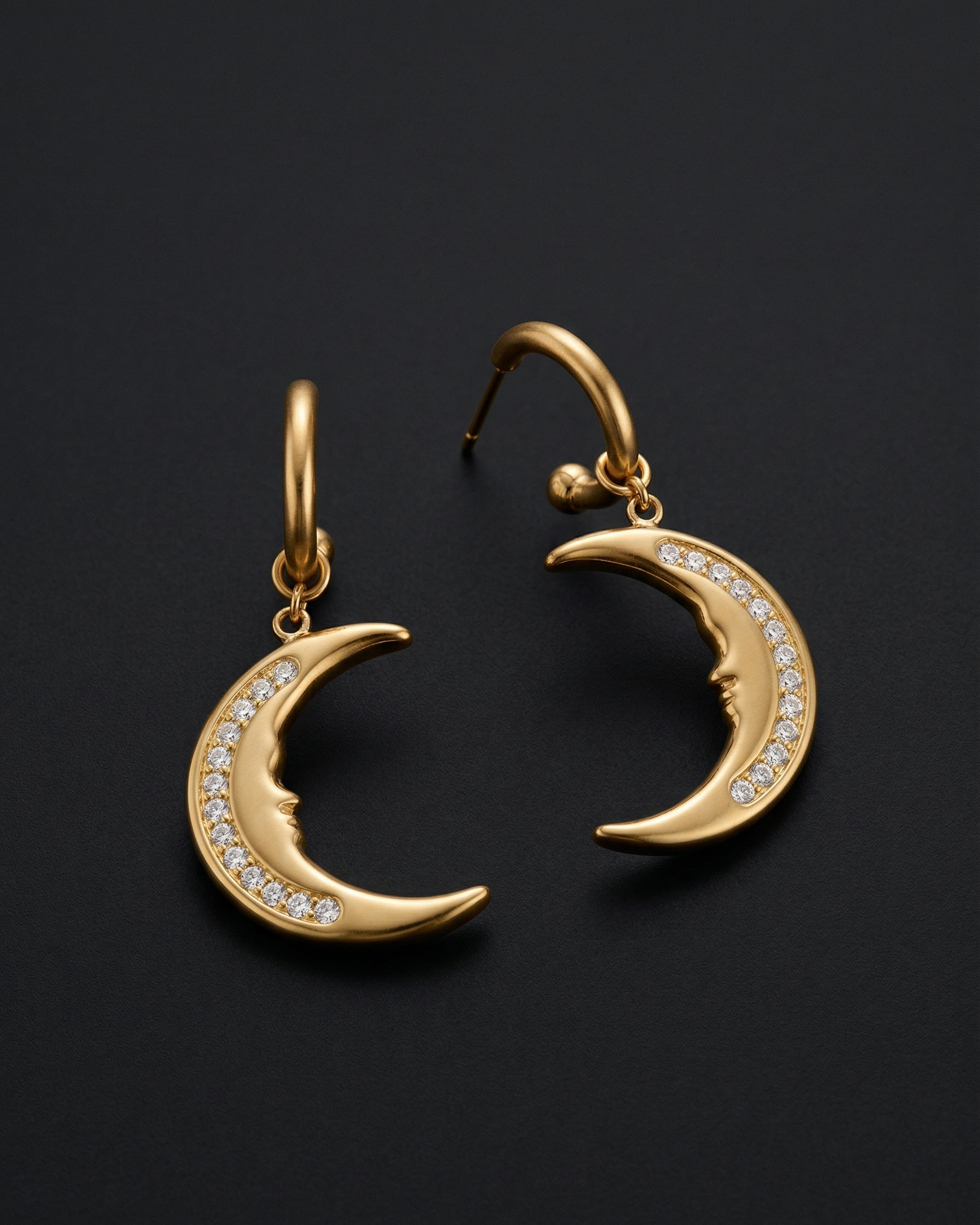 Gold crescent moon earrings with embedded stones on a black background