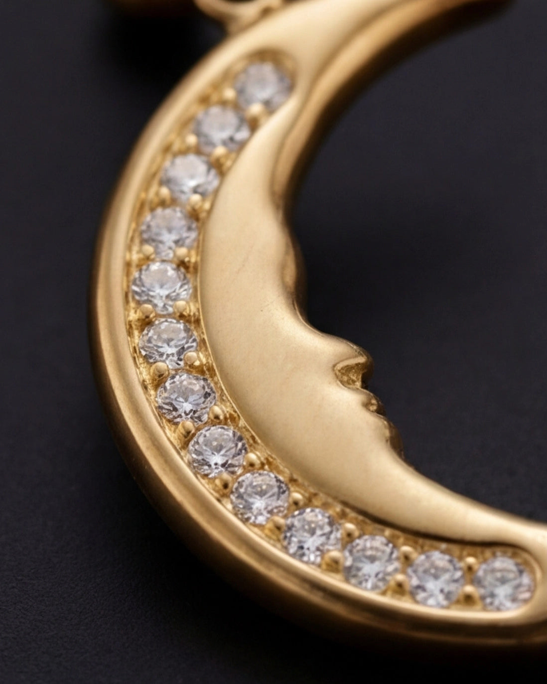 Gold crescent moon pendant with embedded diamonds on a dark background