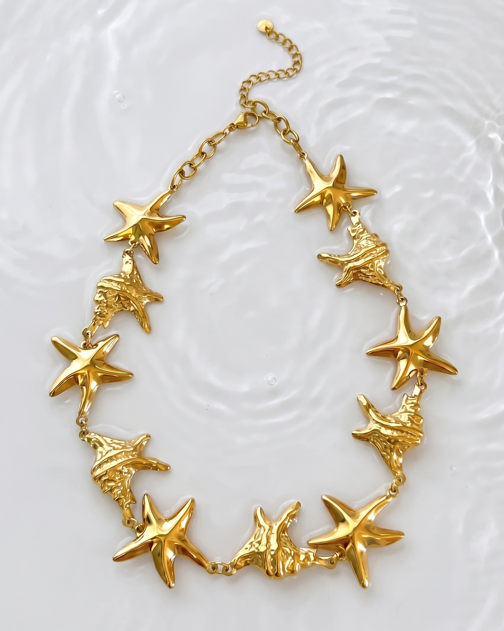 Gold necklace with starfish and shell designs on a textured white background