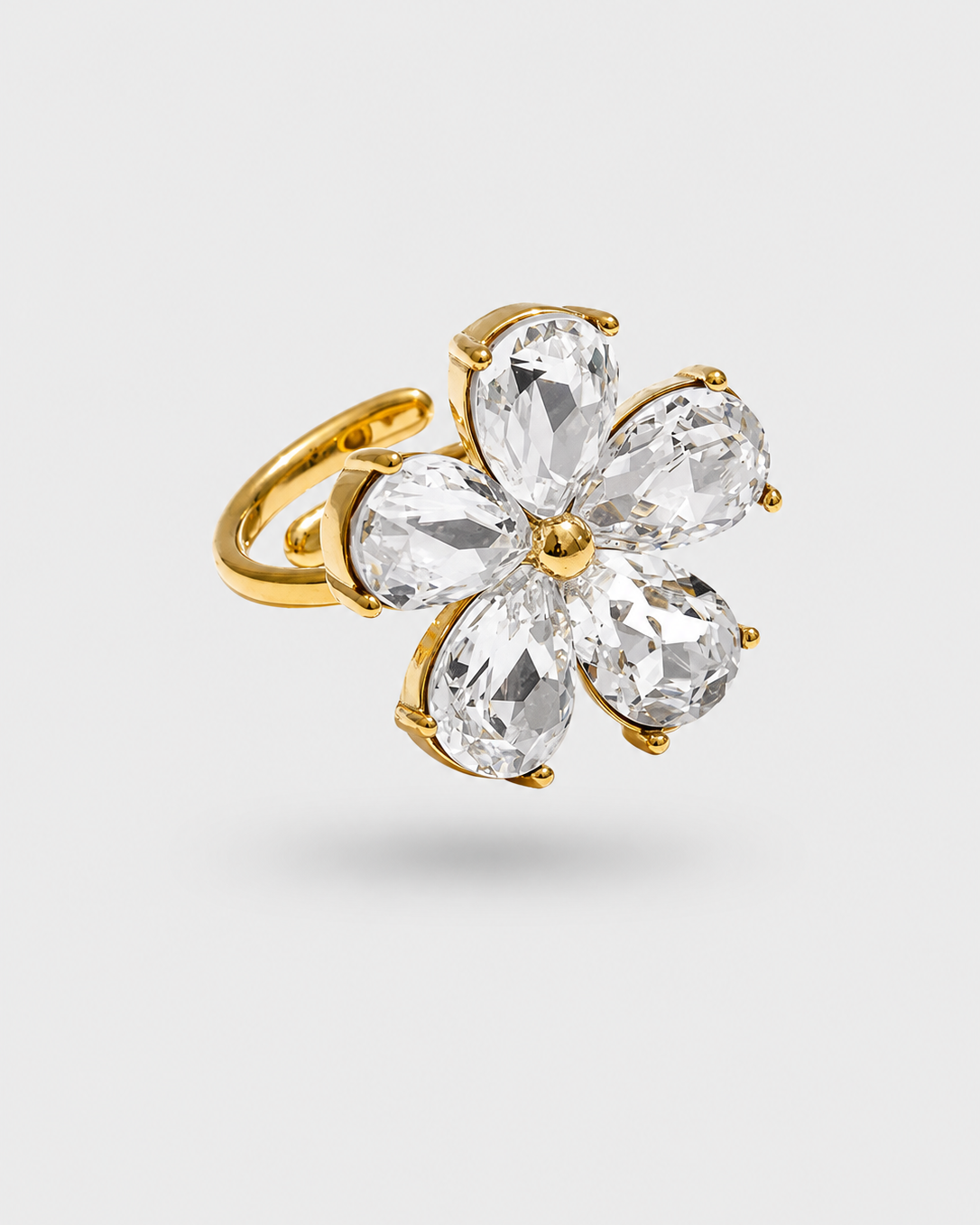 A gold flower-shaped ring featuring five clear, faceted marquise-cut gemstones, shown on a light gray background.