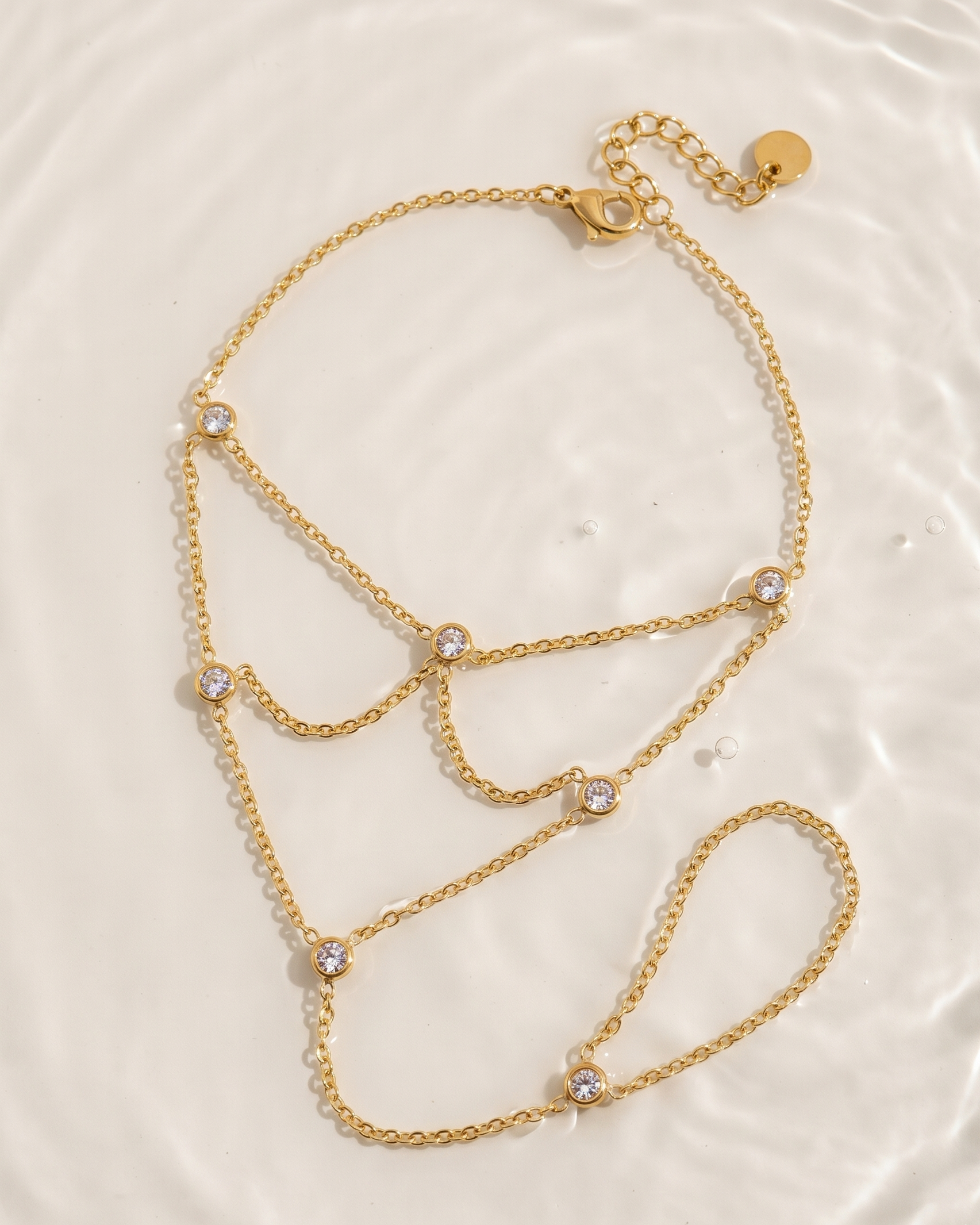 Gold chain necklace with small crystals on a light beige background