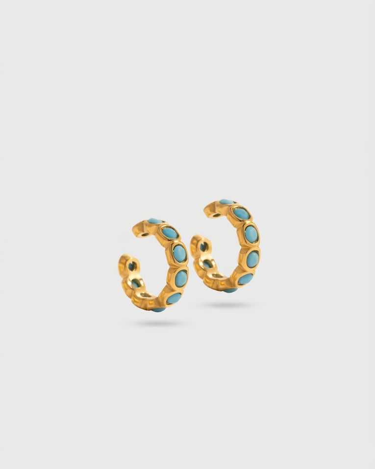 Gold hoop earrings with turquoise stones on a light gray background