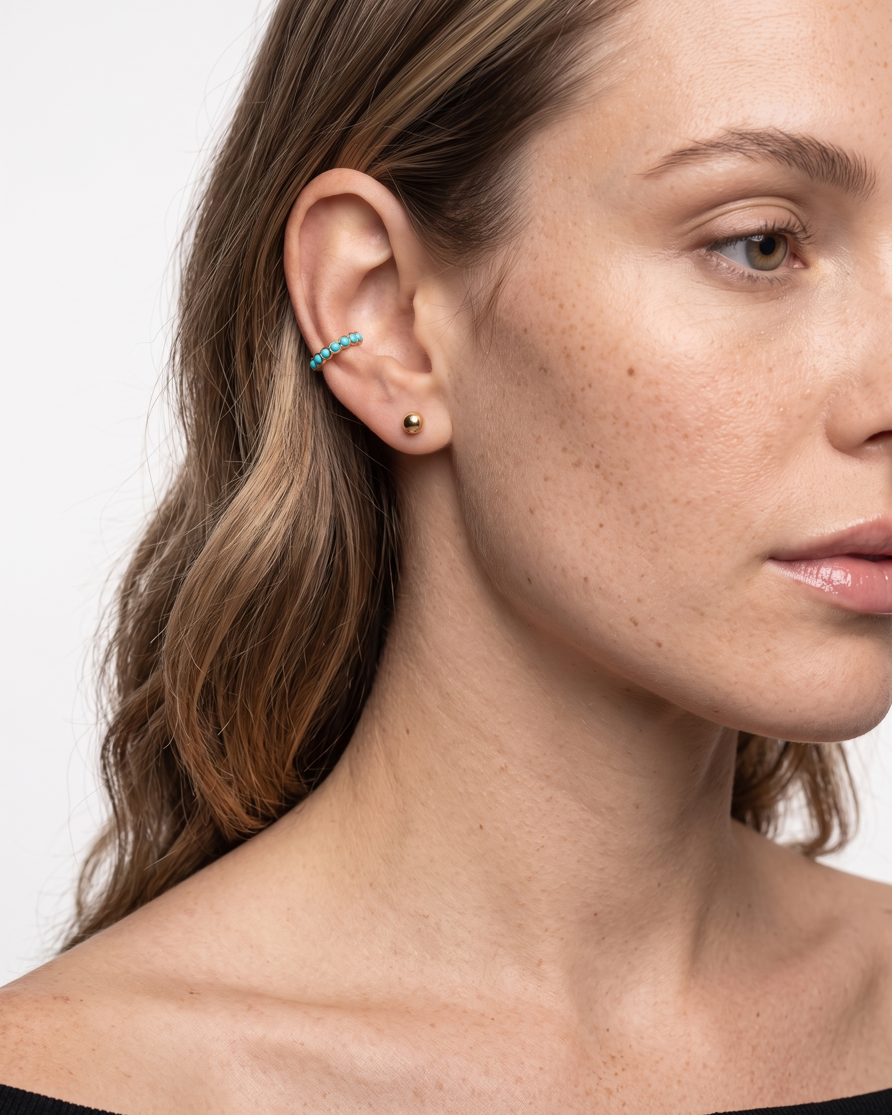 Close-up of a woman wearing a turquoise earring on a plain background