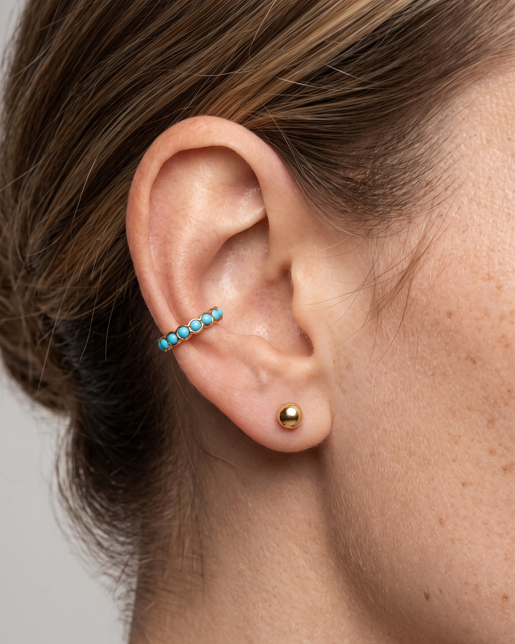 Close-up of an ear with turquoise beaded earring and gold stud earring on a neutral background