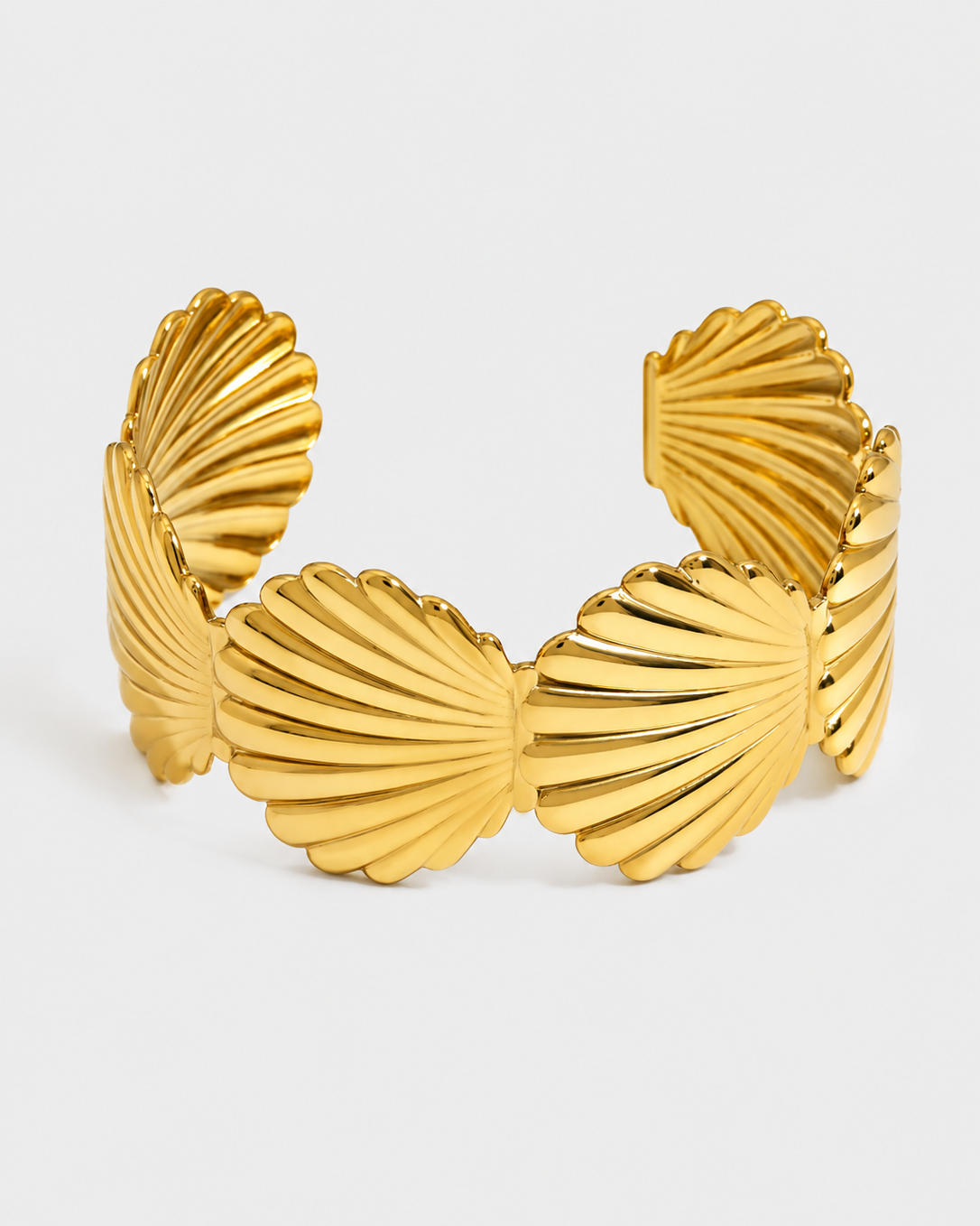 A wide gold cuff bracelet designed with a ribbed, fan-like shell motif, photographed on a clean light gray background.