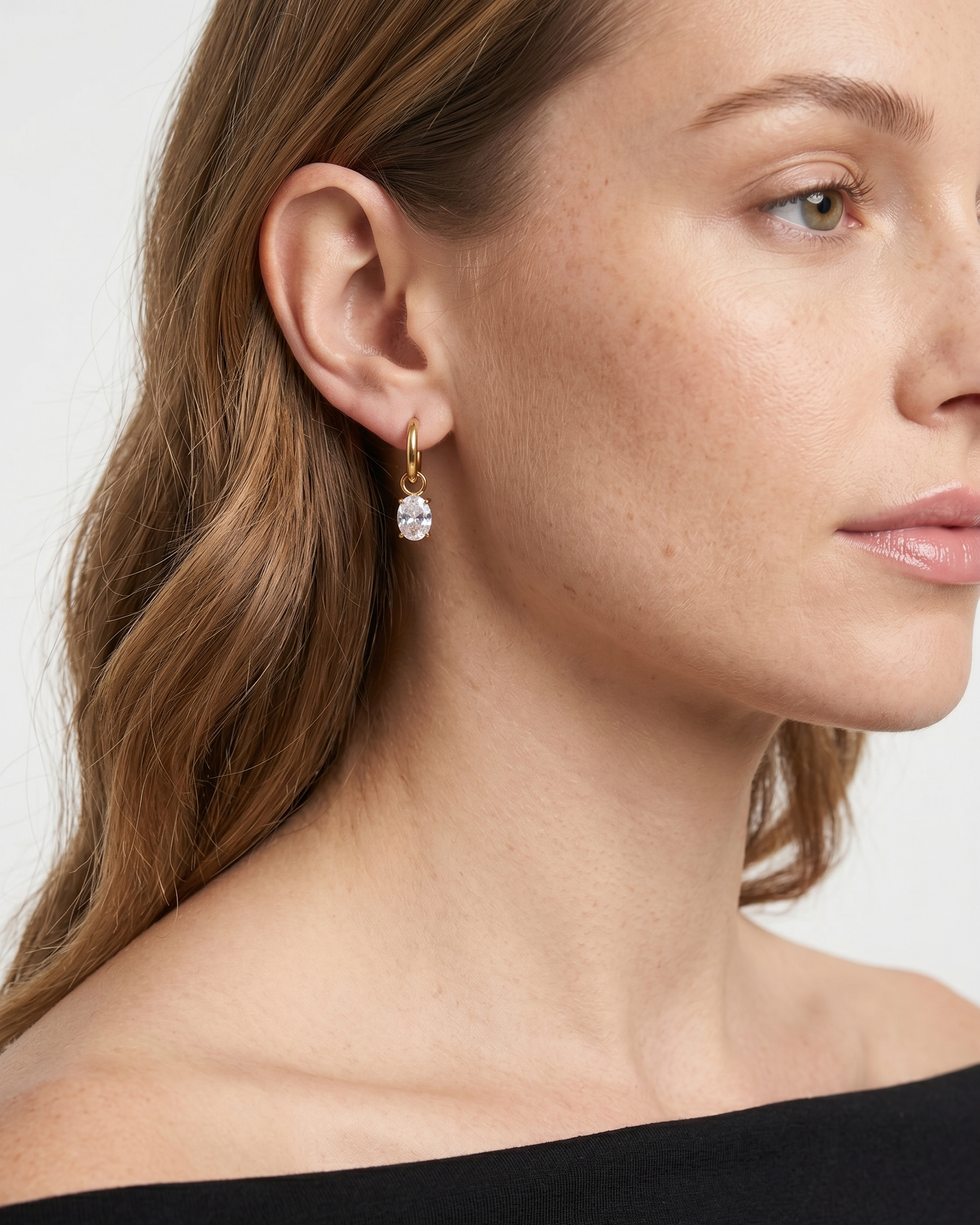 Close-up of a woman wearing gold earrings with a clear gemstone against a neutral background