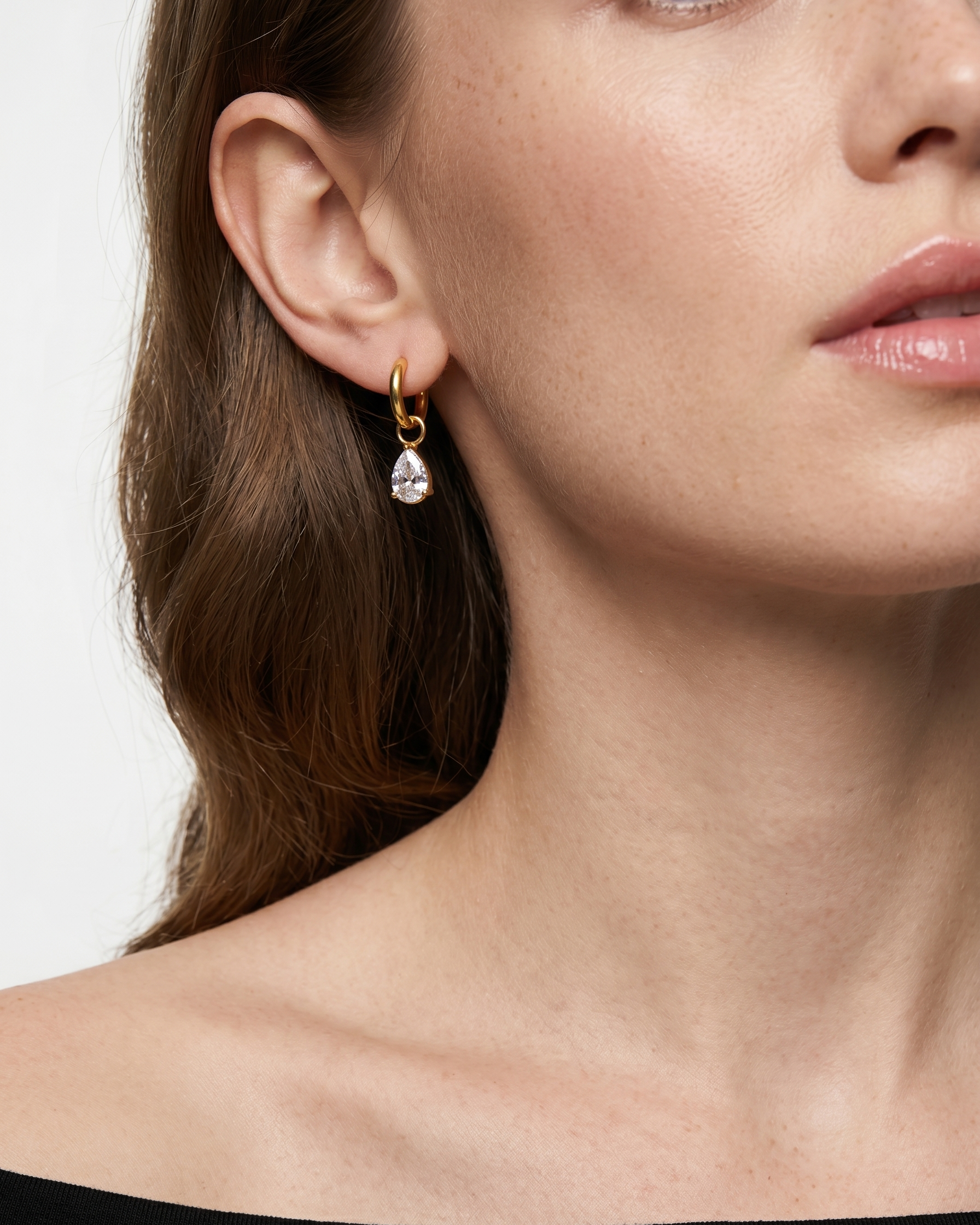 Close-up of a woman wearing a gold earring with a clear gemstone.