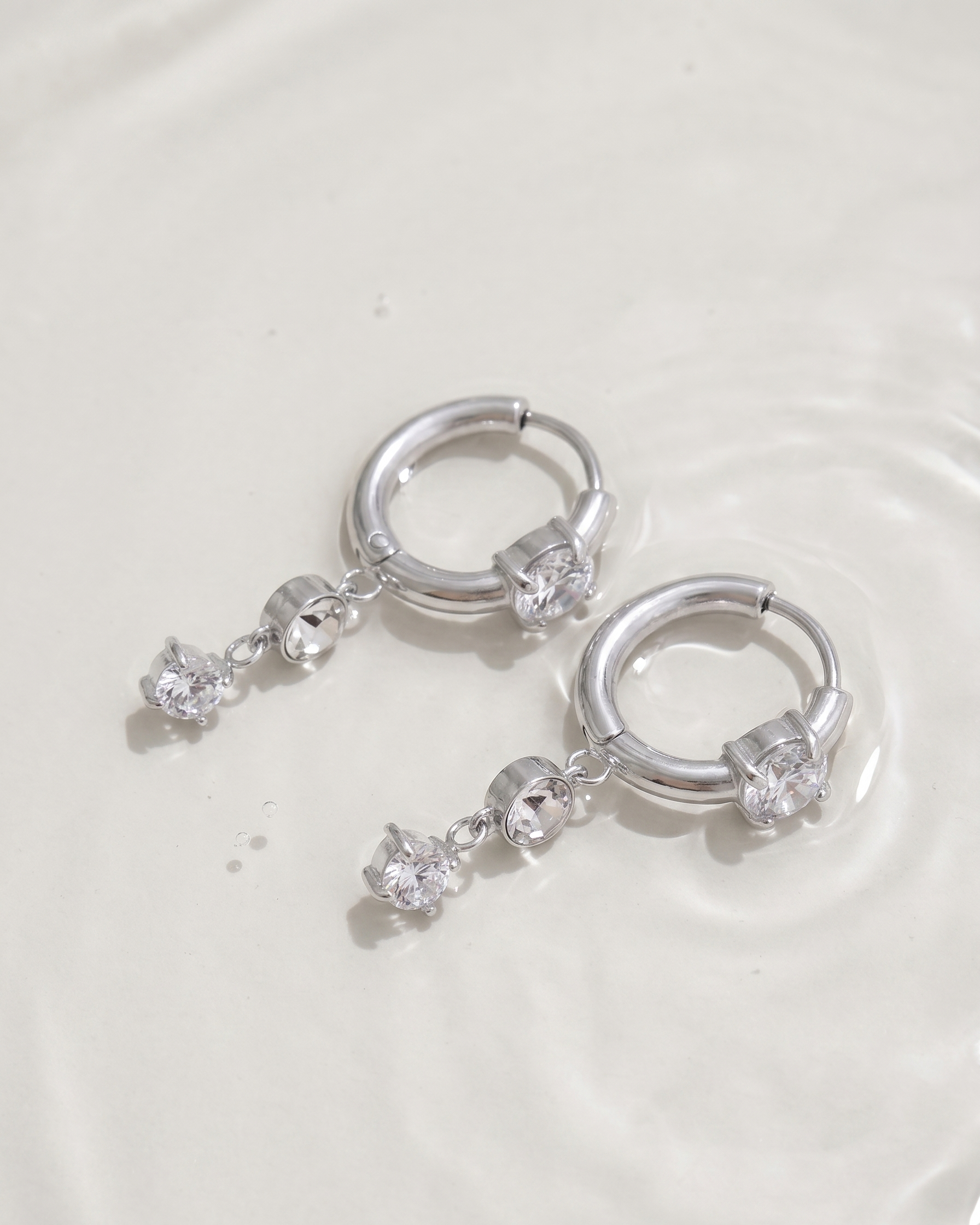 Silver hoop earrings with dangling crystals on a light gray background