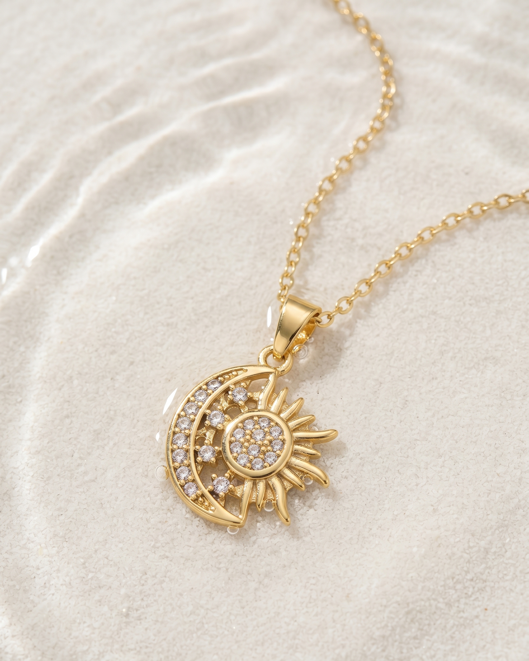 Gold necklace with sun and moon pendant on a textured beige surface