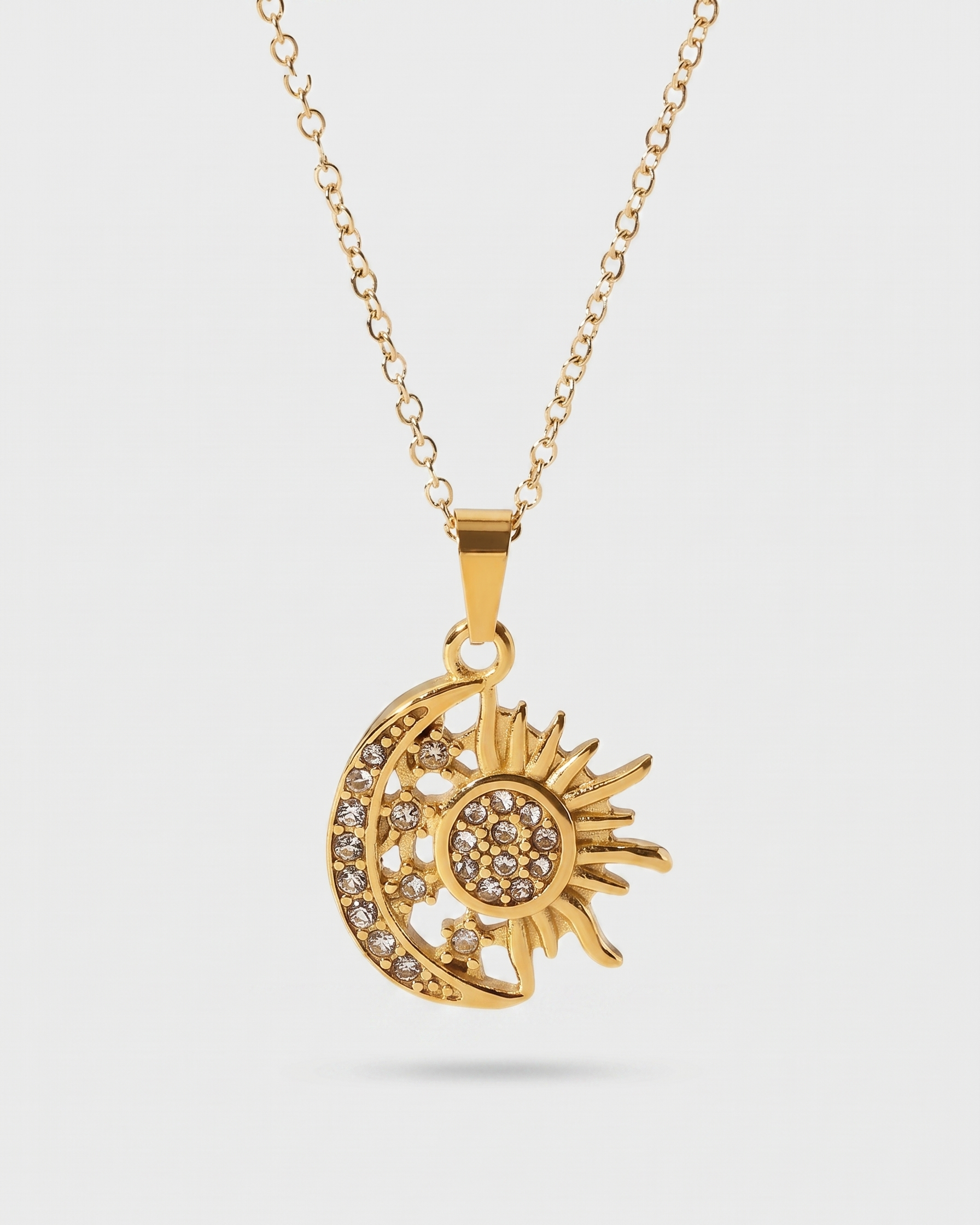 Gold necklace with a sun and moon pendant on a light gray background