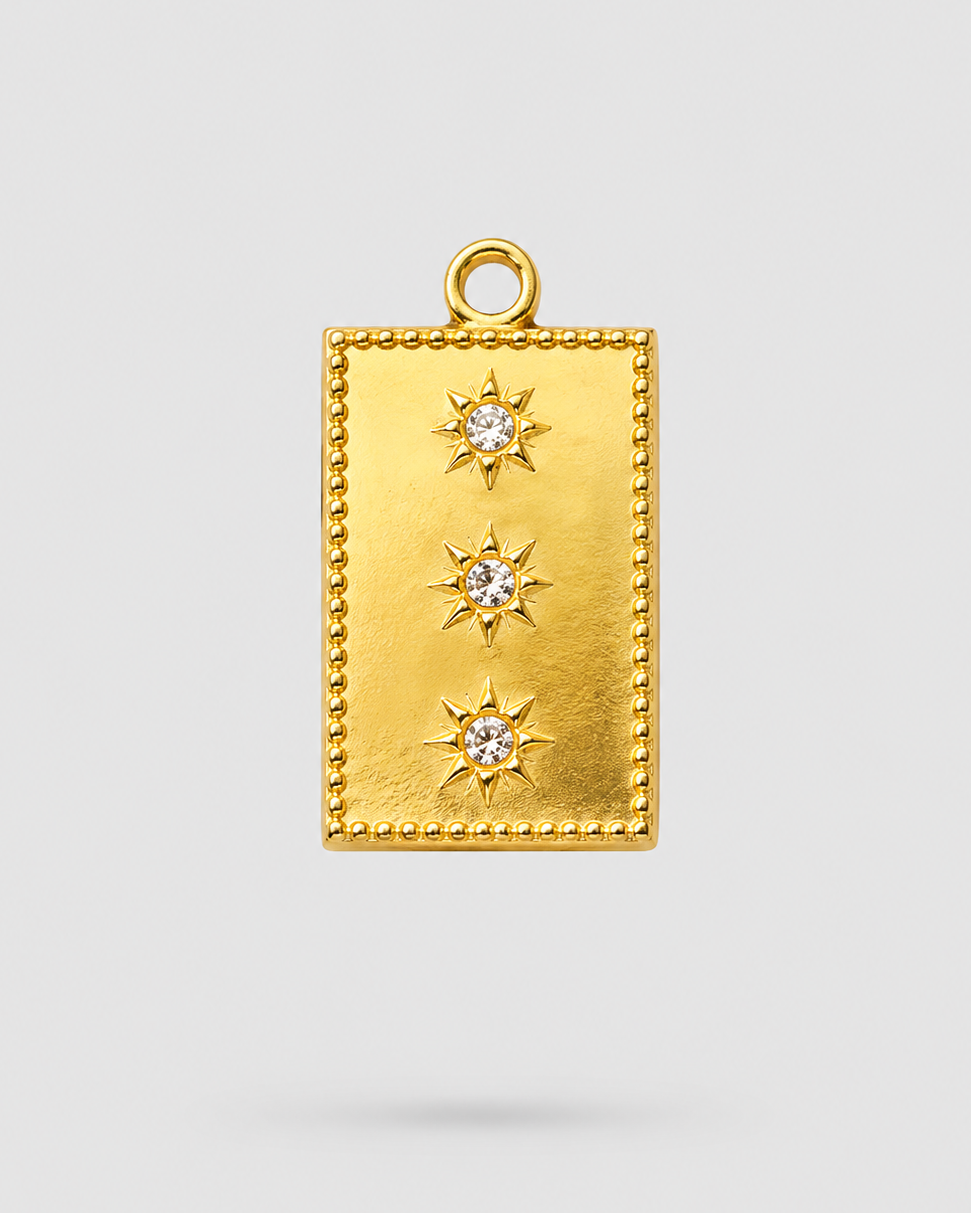 A gold rectangular pendant charm with a beaded border, three vertical rows of starburst motifs, and a clear central gemstone in each star, shown on a light gray background.