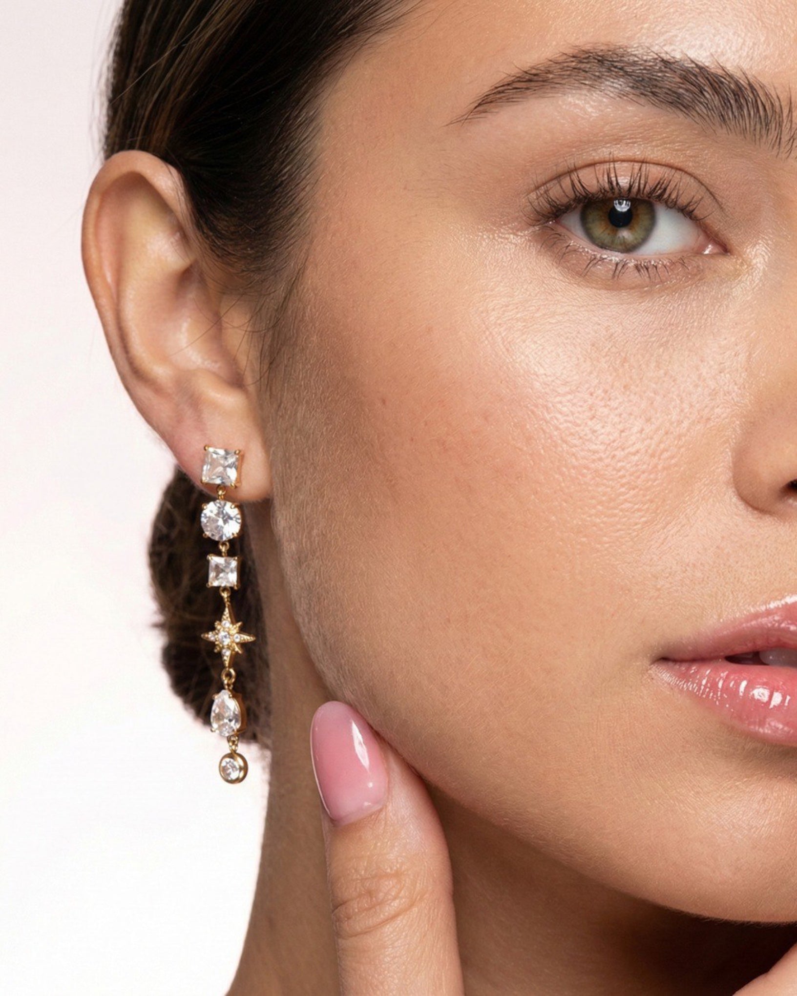 Close-up of a woman wearing a pair of dangling earrings with a neutral background
