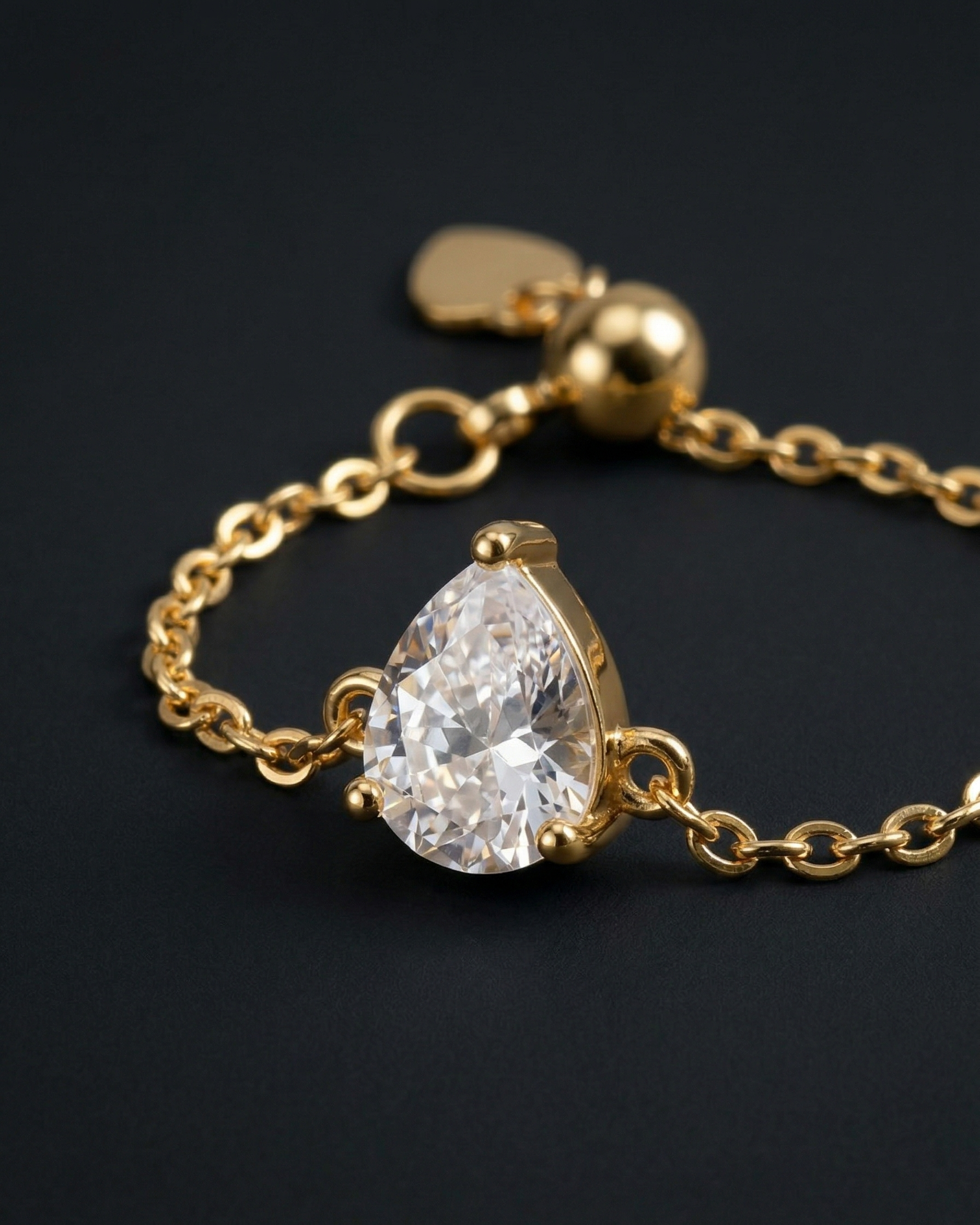 Gold bracelet with a teardrop-shaped diamond on a black background