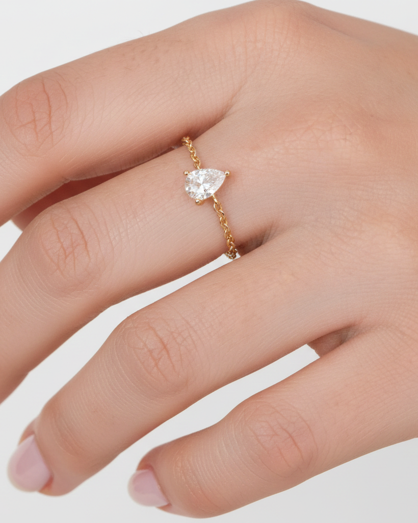 Gold ring with a pear-shaped diamond on a hand against a light gray background