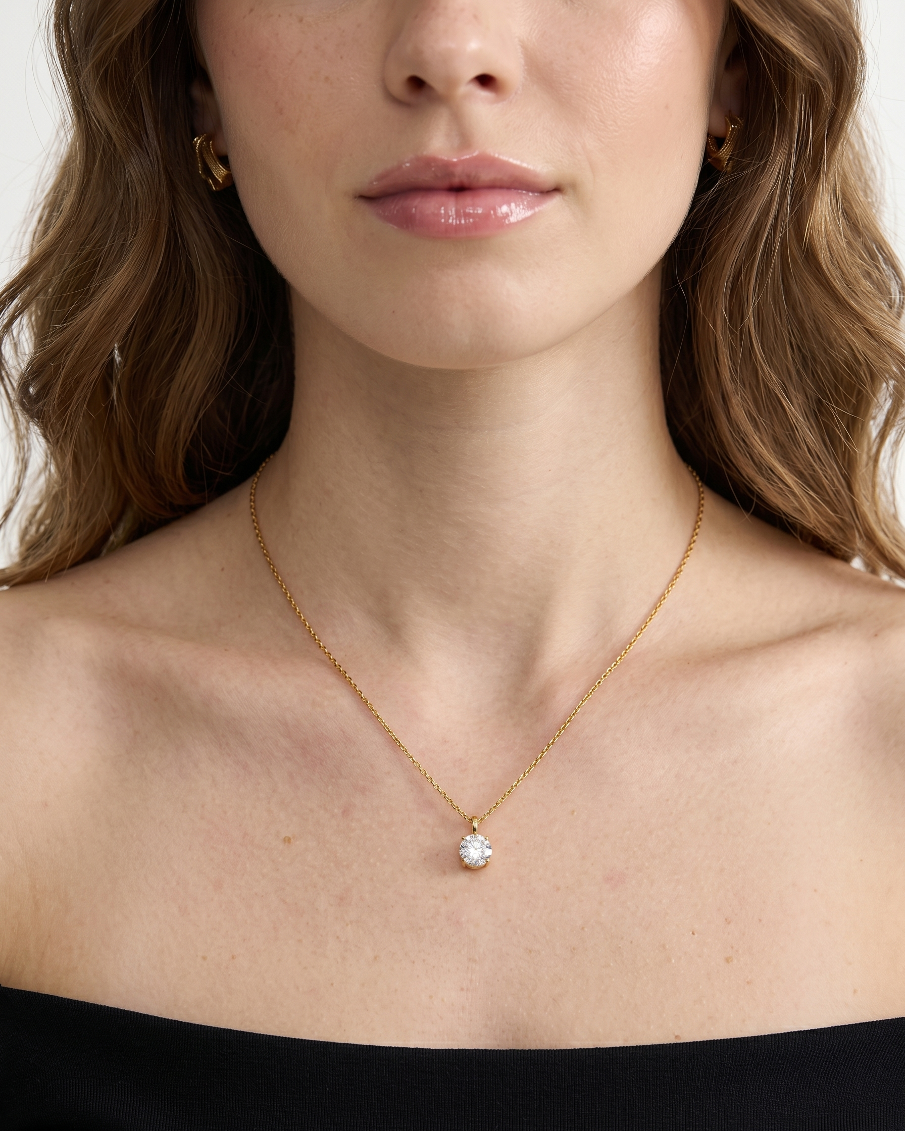 Woman wearing a gold necklace with a small pendant against a neutral background