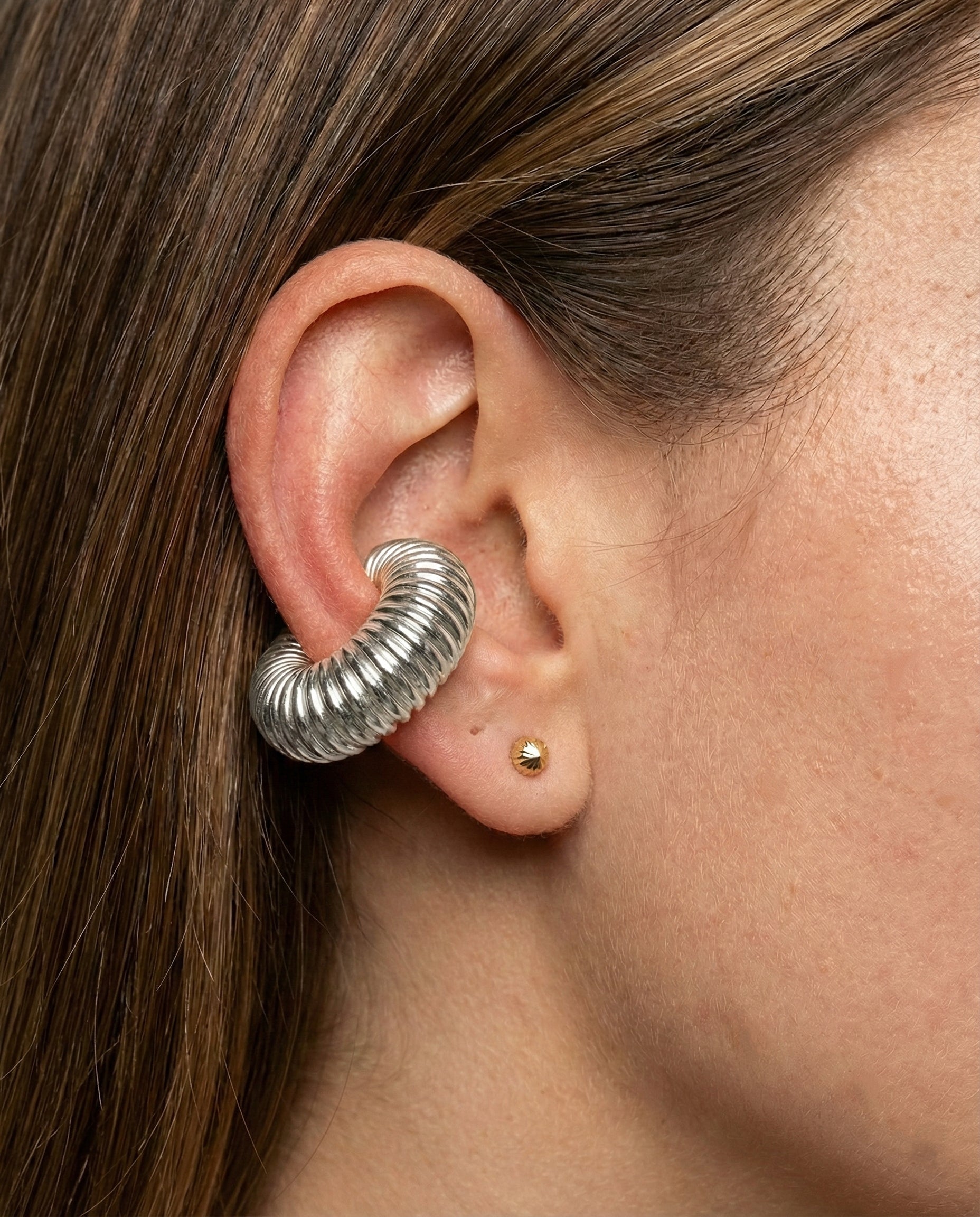 Close-up of an ear wearing a silver spiral earring with a gold stud.