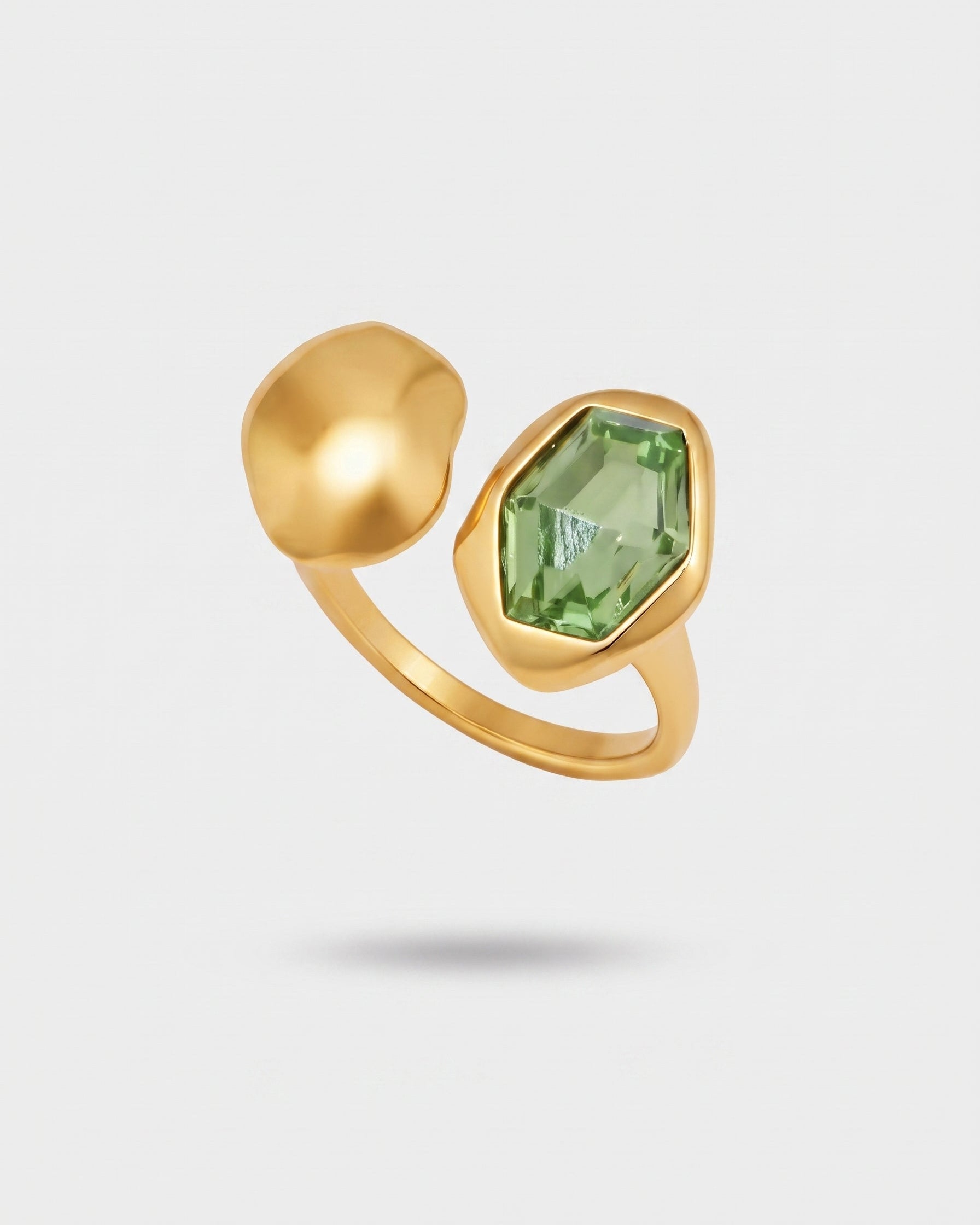 A gold ring featuring a large, faceted green gemstone in a geometric bezel setting alongside a smooth, rounded gold dome accent, shown on a light gray background.