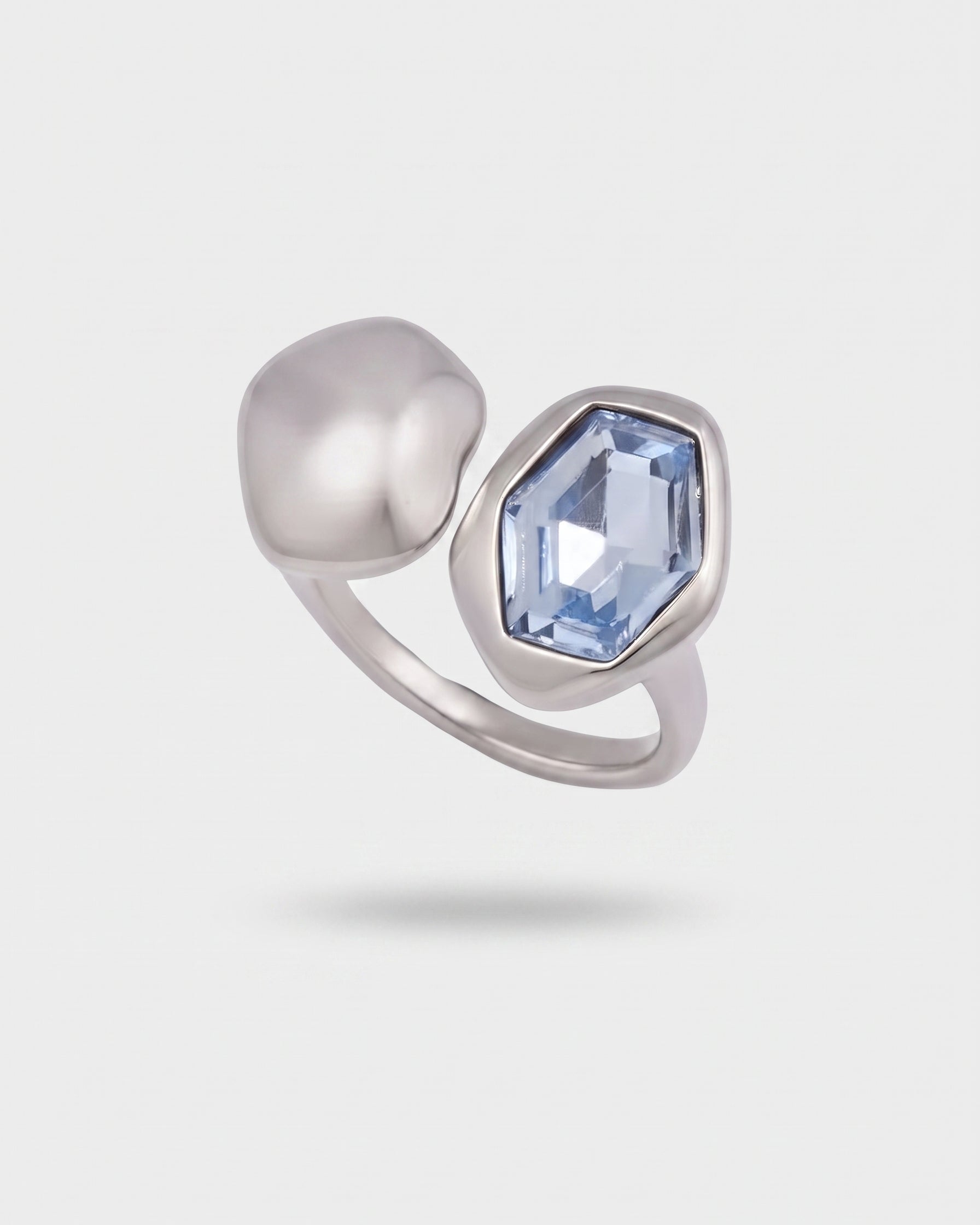 A silver-toned ring featuring a large, polished dome-shaped bead on one side and a faceted, elongated light blue gemstone on the other, set against a light gray background.