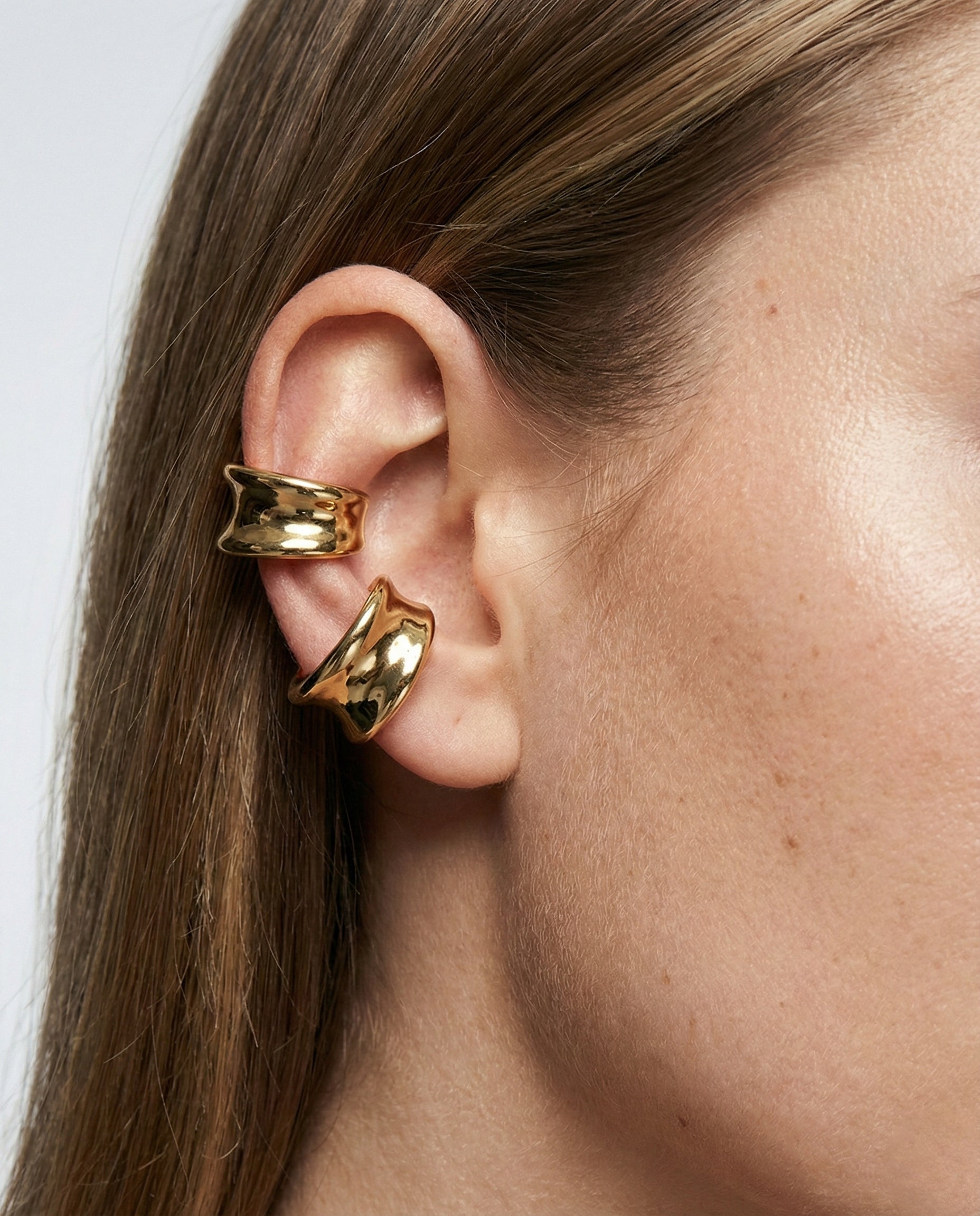 Gold earrings worn by a person with a neutral background