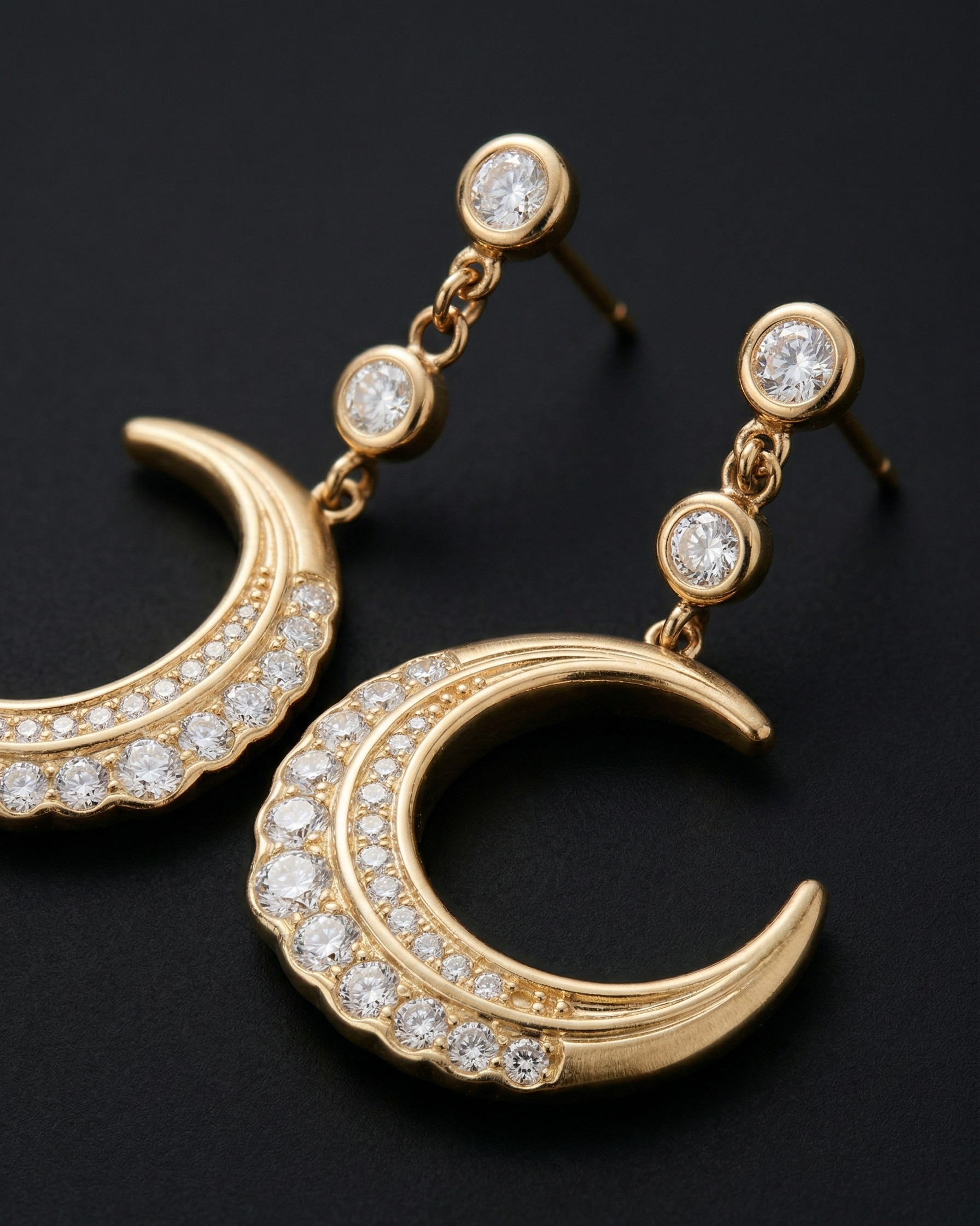 Gold crescent moon earrings with embedded diamonds on a black background