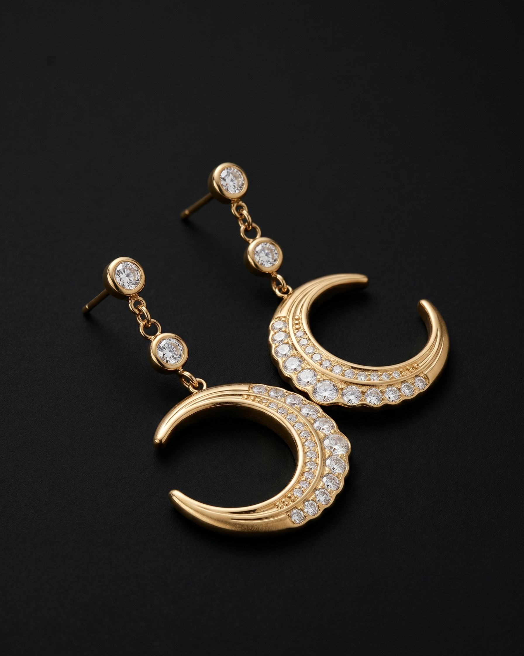 Gold crescent moon earrings with embedded stones on a black background