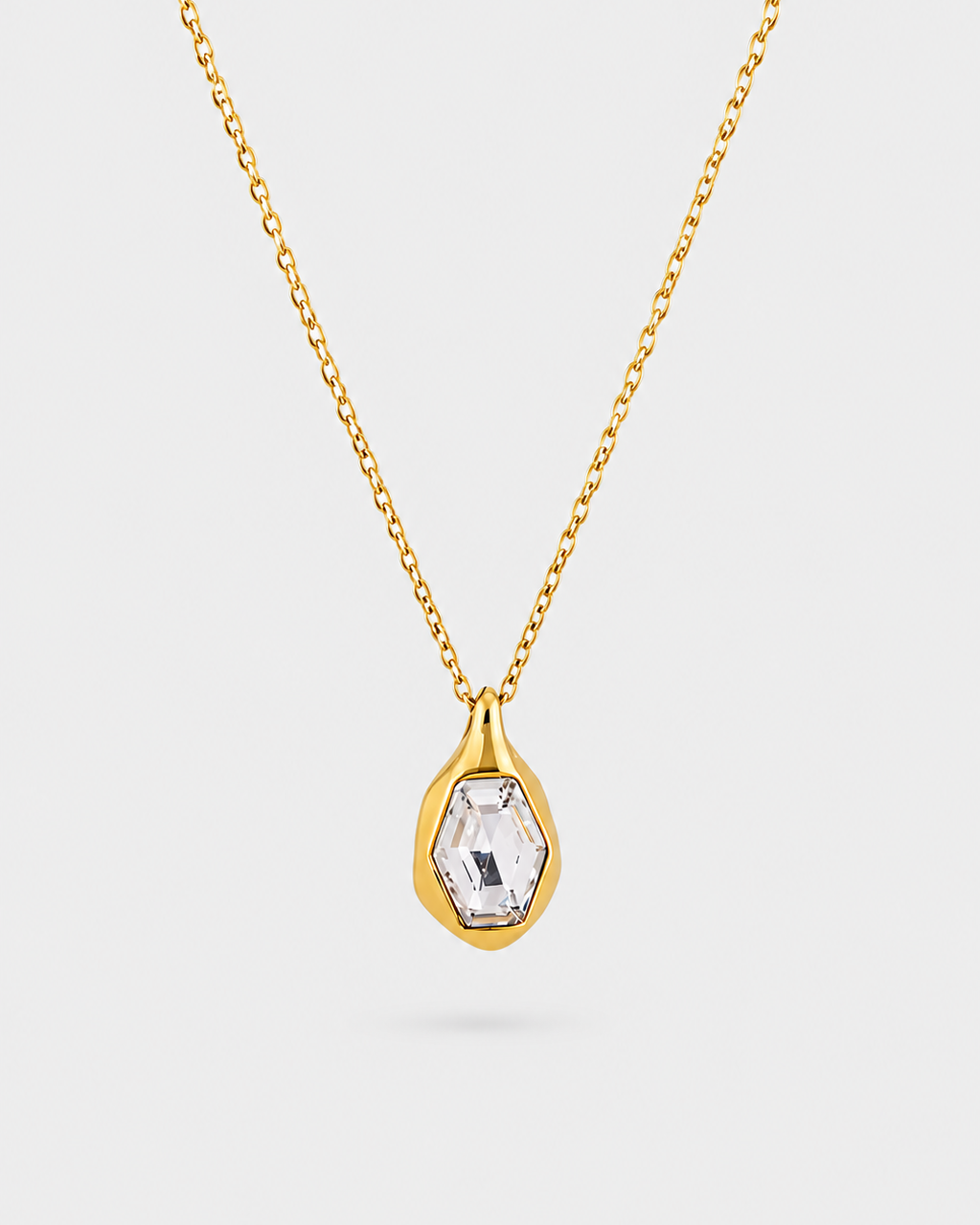A gold chain necklace with a teardrop-shaped pendant featuring a clear faceted gemstone in a gold bezel setting, shown against a light gray background.
